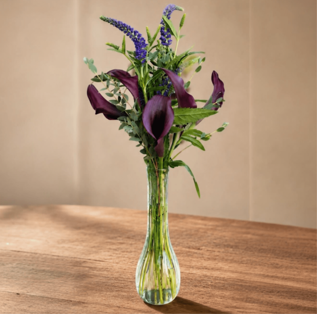 Midnight Calla - An elegant calla lily arrangement with seasonal blooms and fresh greenery in a clear glass vase. Perfect for any refined occasion.
