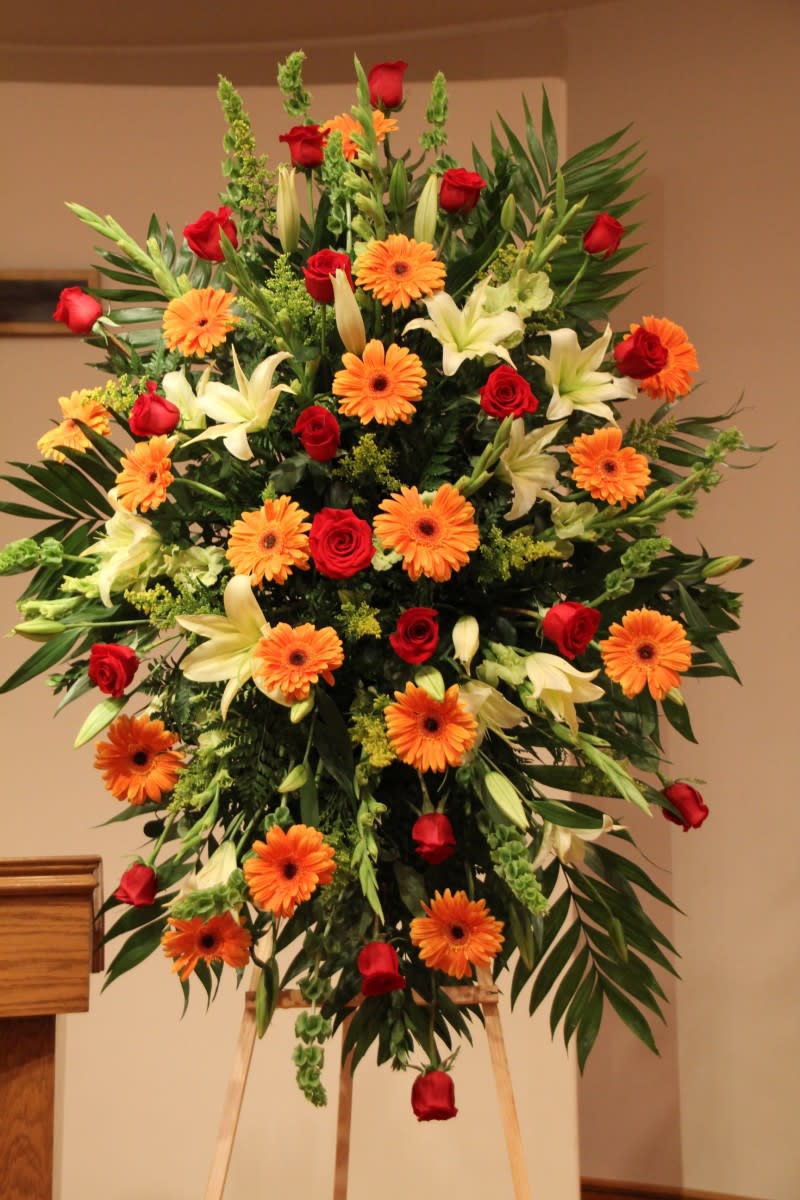 Large standing floral spray with red roses, orange gerberas, and white lilies