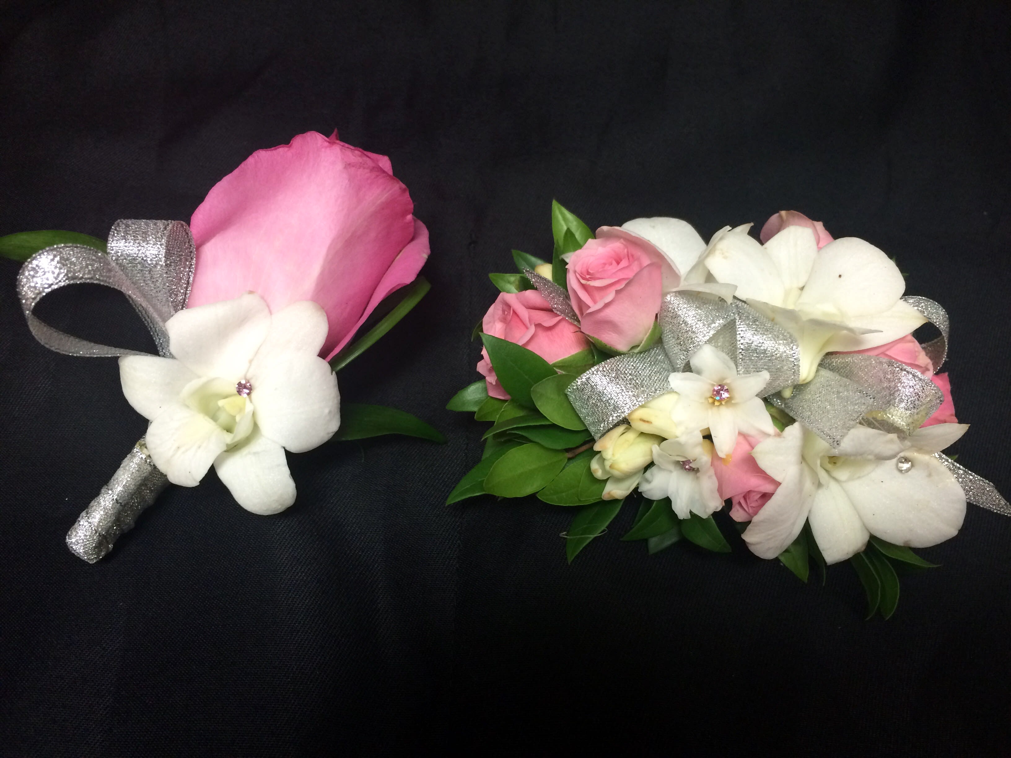 Pink and white floral corsages with silver ribbon on a black background