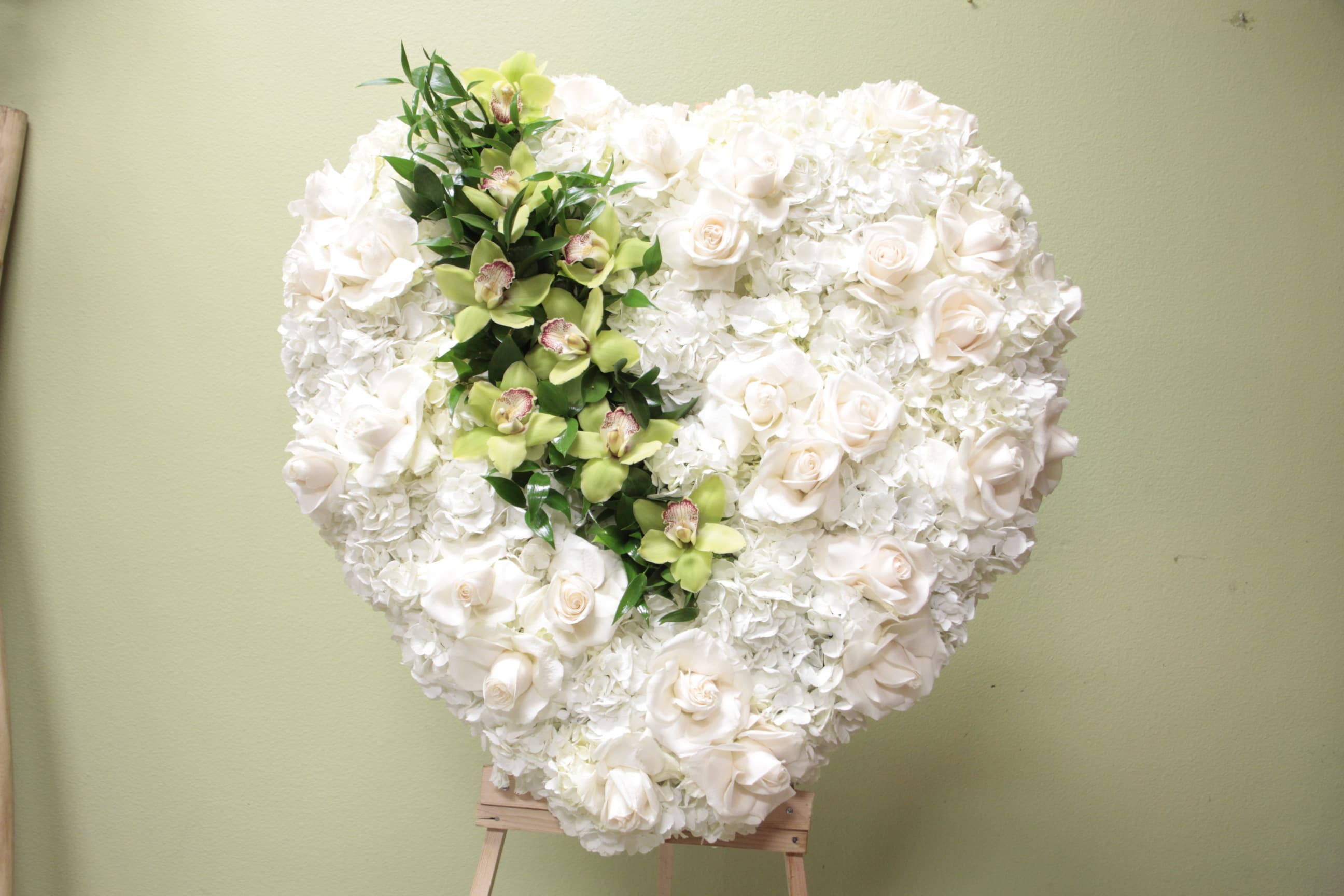Heart-shaped white floral arrangement with a green orchid accent