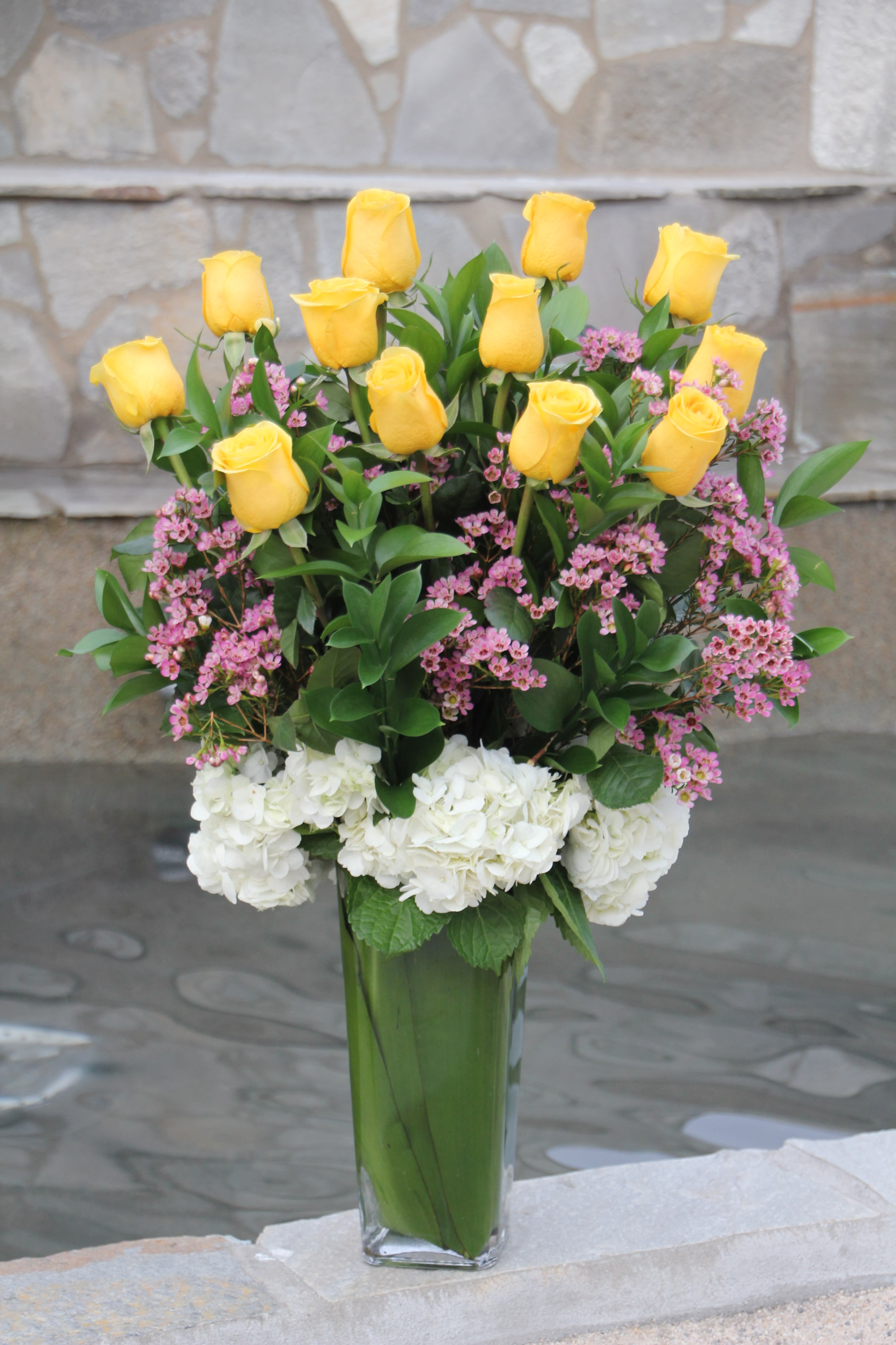 Yellow roses and pink flowers in a tall glass vase