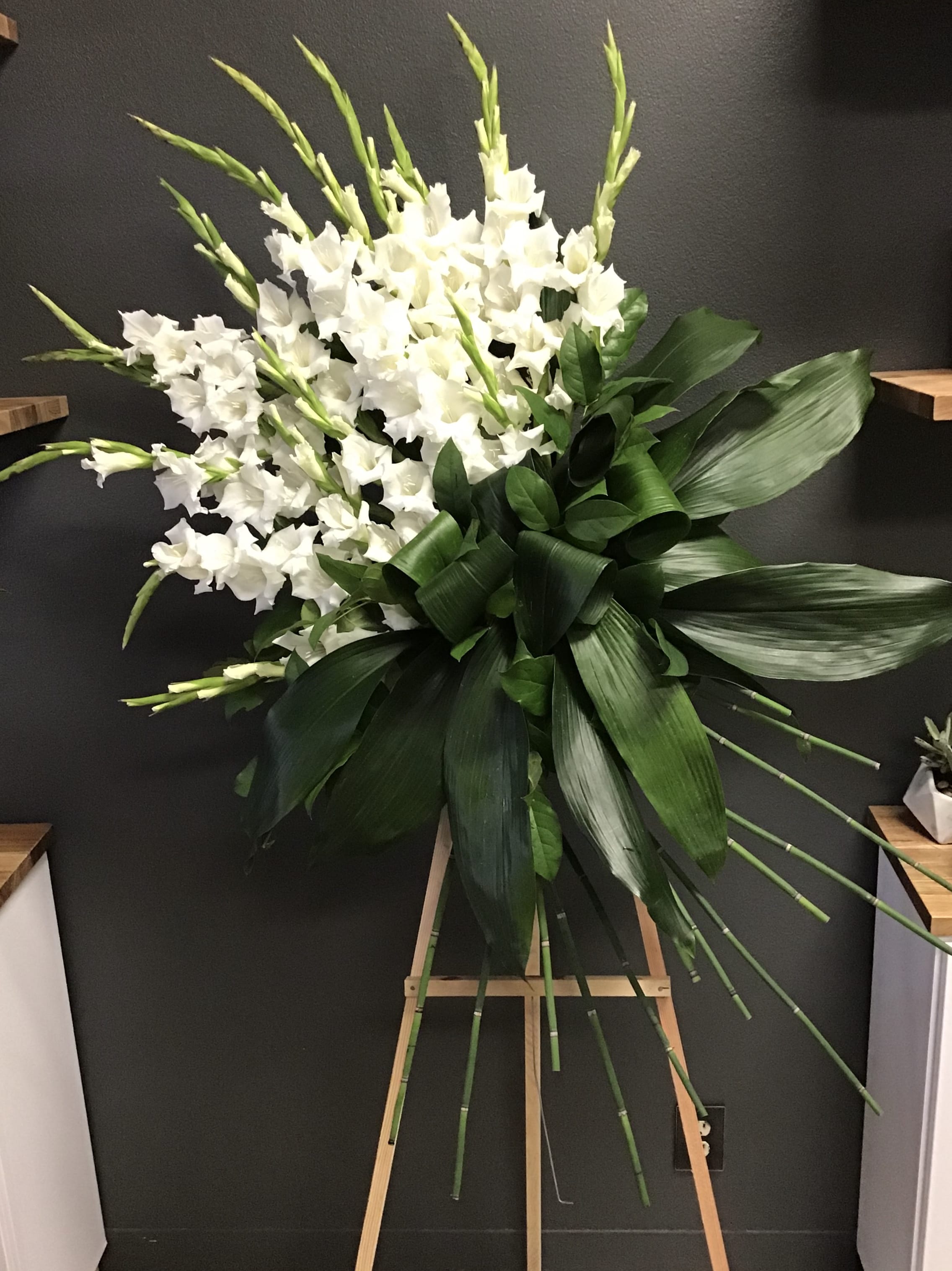 White gladiolus arrangement with large green leaves on an easel