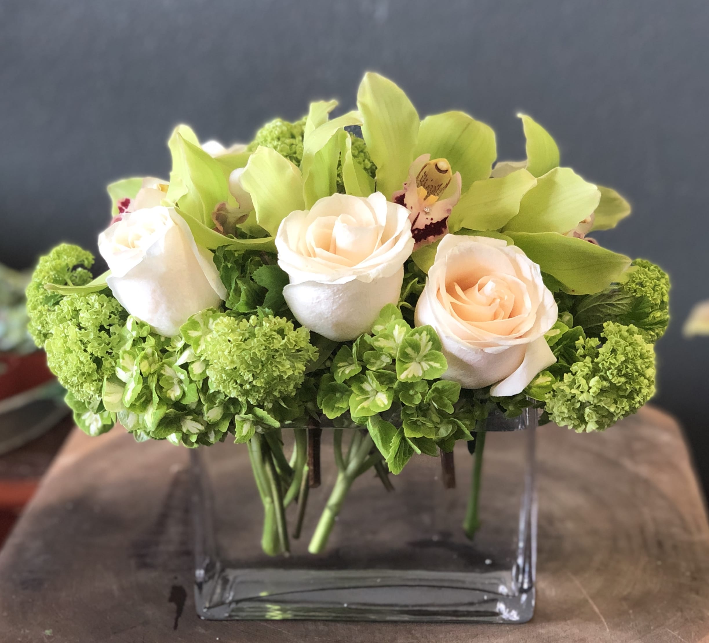 Compact bouquet of pale peach roses and green orchids in a clear glass vase