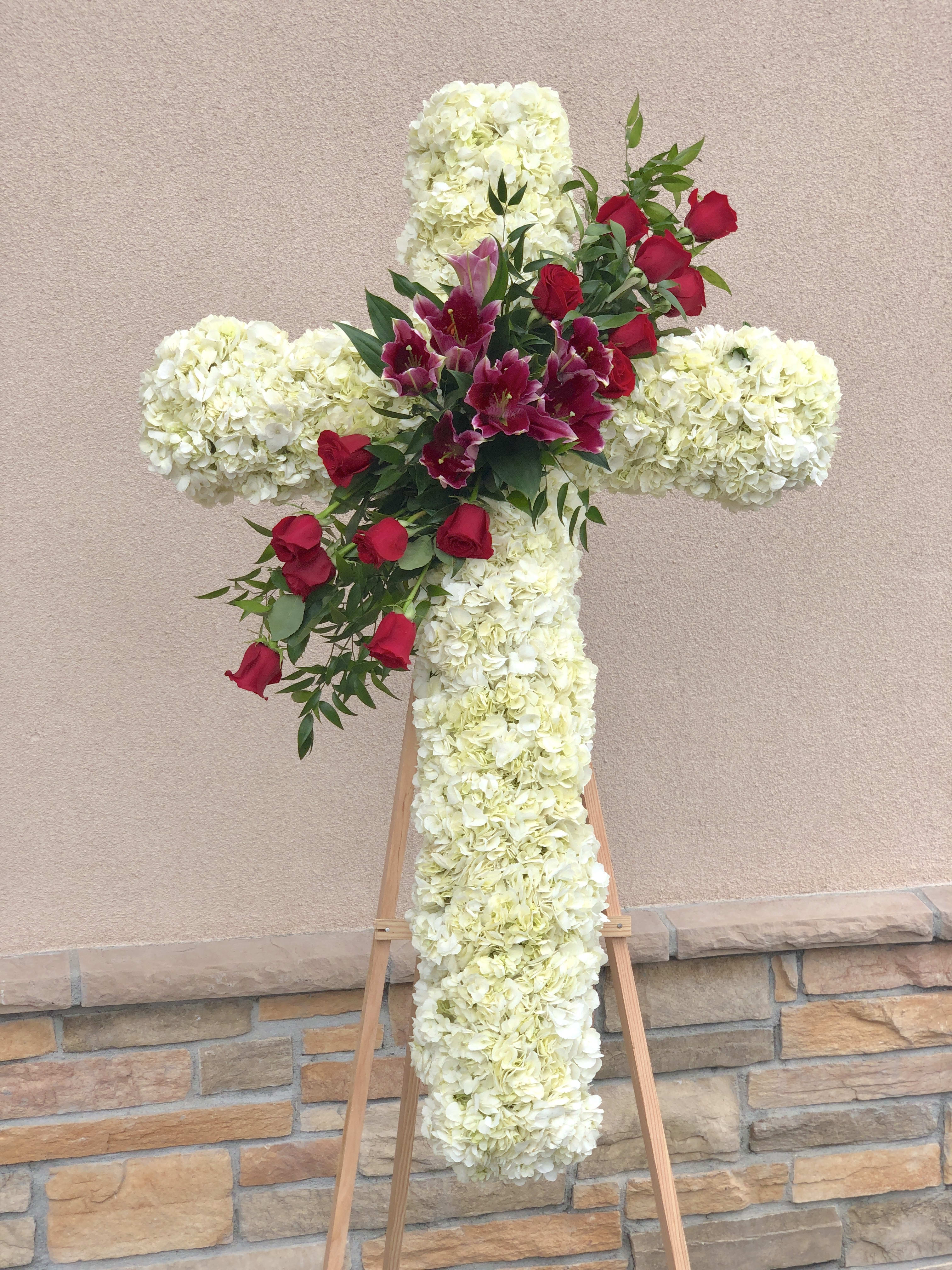 Blessing Cross - Commemorate fidelity with this standing spray cross of white blossoms adorned with fragrant lilies and fresh red roses. It’s a display that remembers faith, hope and charity. Stndard price is for 36" cross.