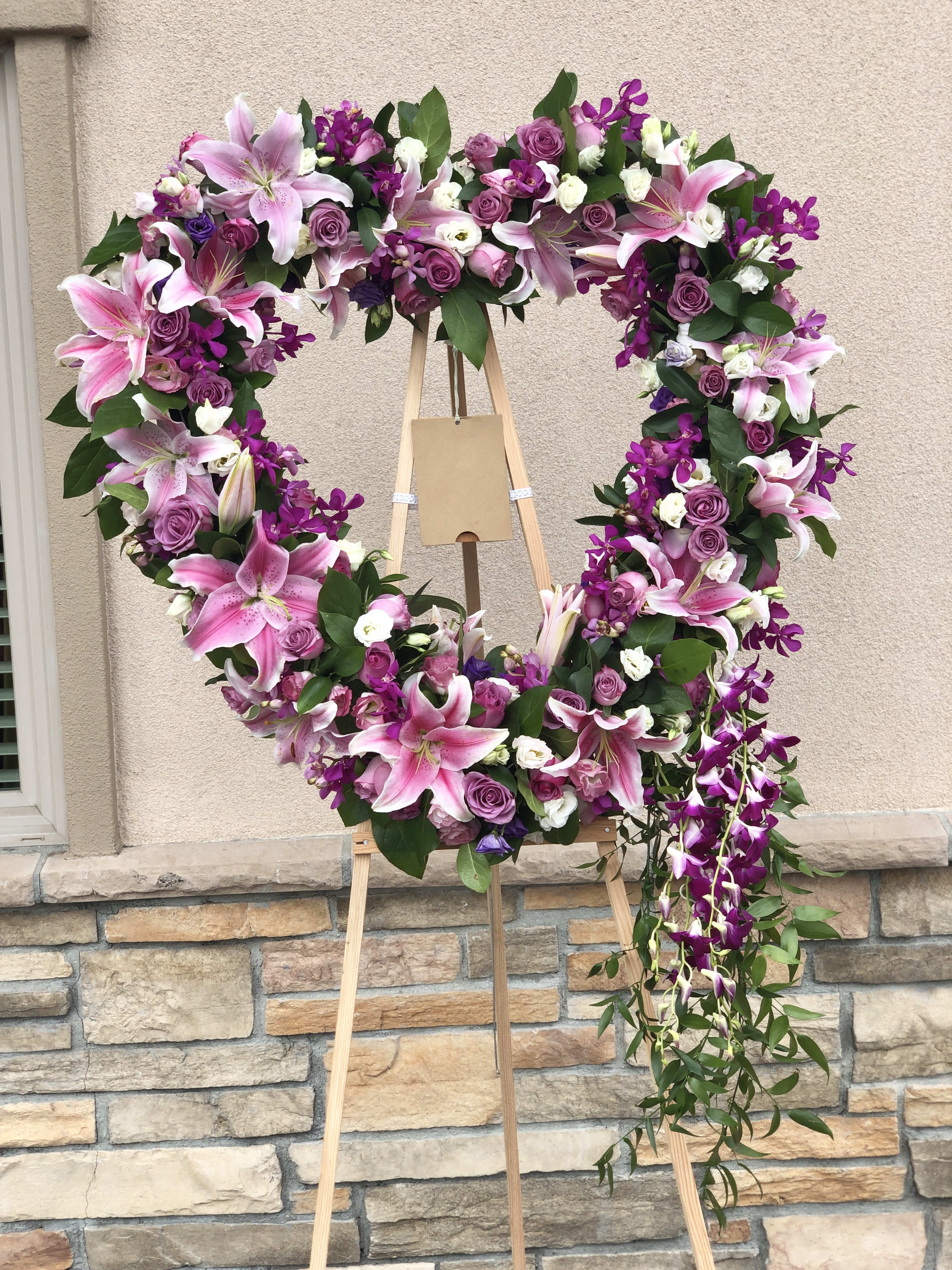 Heart-shaped floral wreath with pink lilies, purple roses, and orchids on an easel