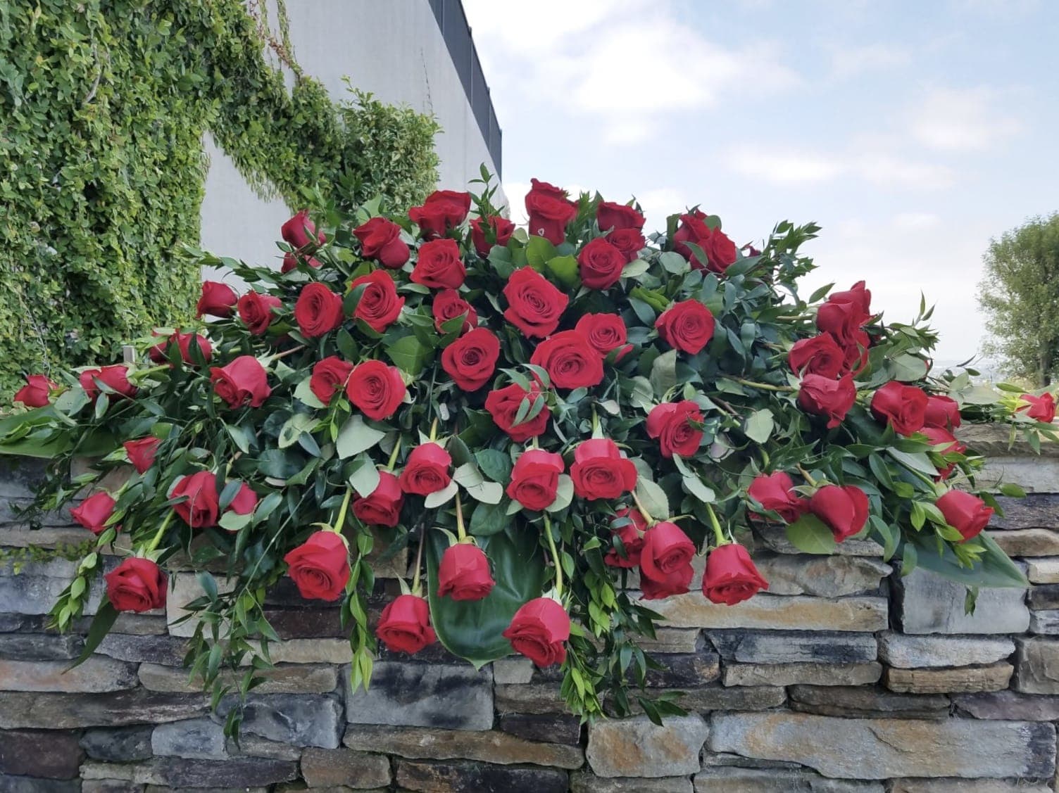 Large arrangement of red roses draped over a stone wall