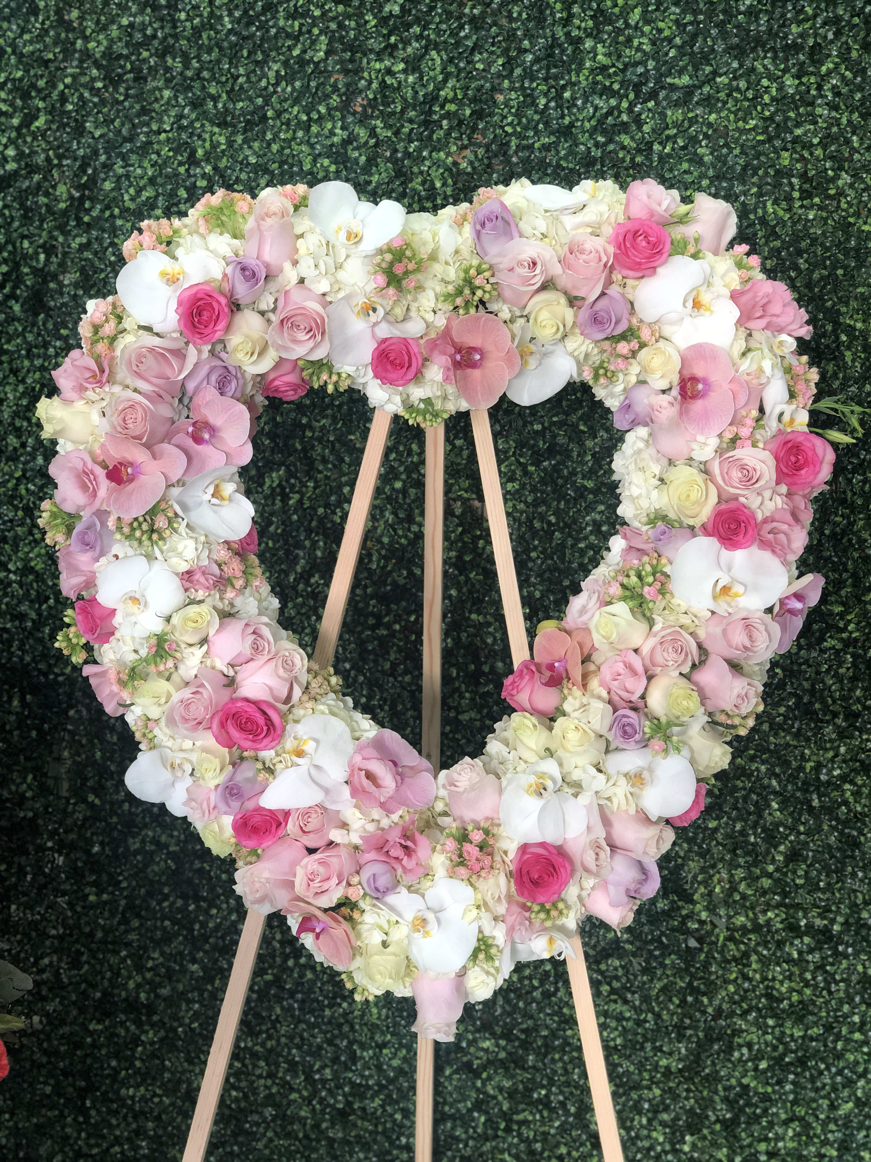 Heart-shaped floral wreath of pink, white, and lavender blooms on a wooden stand