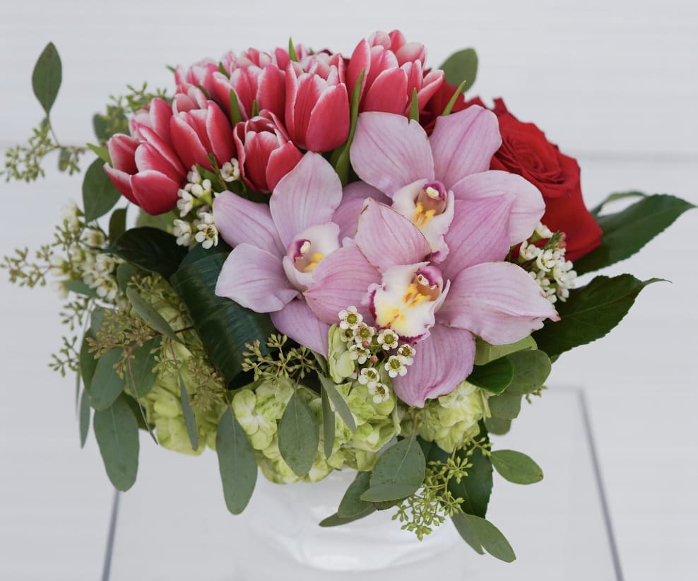 Bouquet of pink tulips, orchids, and red roses in a white vase