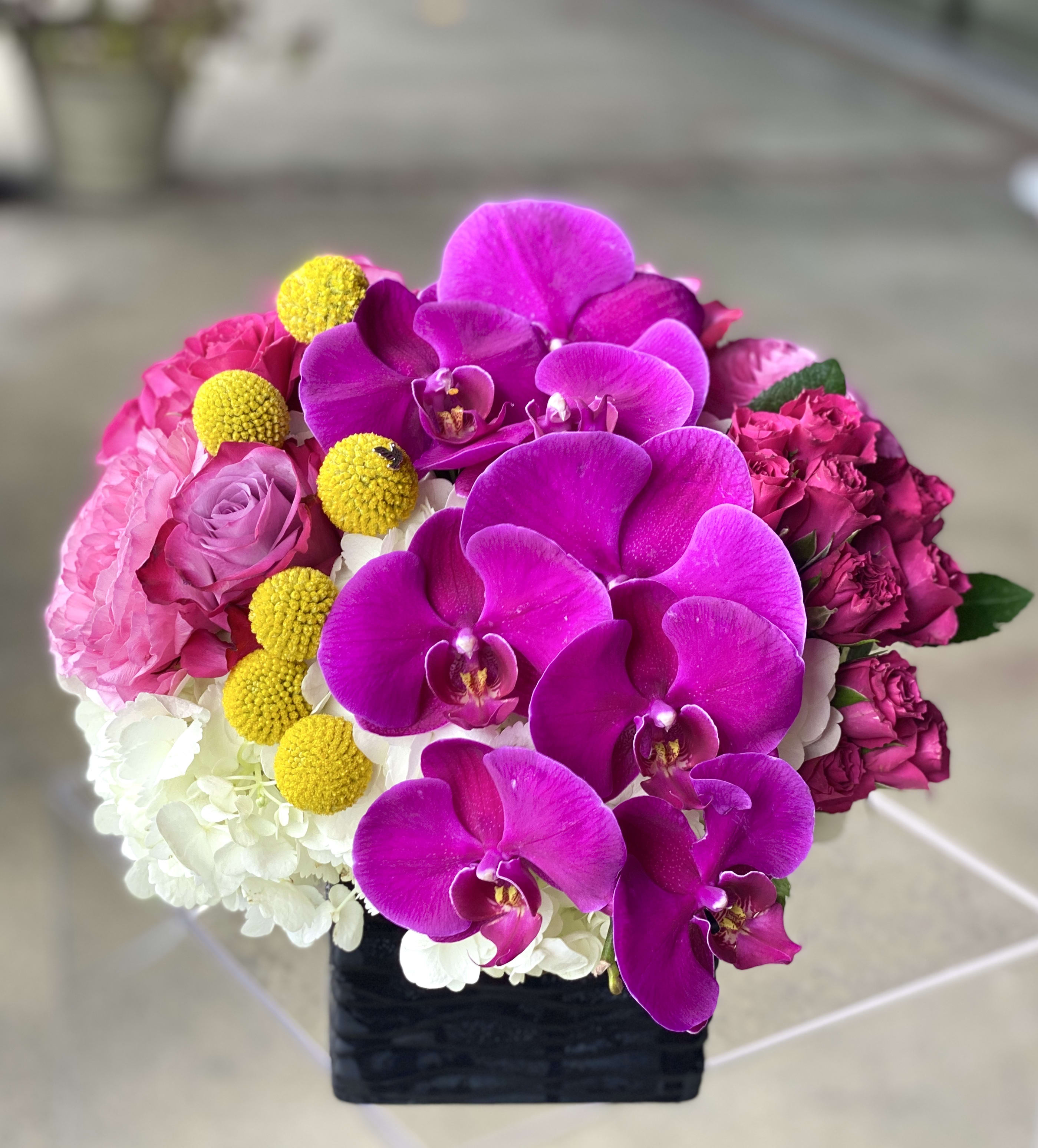 Bright pink orchid and rose arrangement in a black square vase
