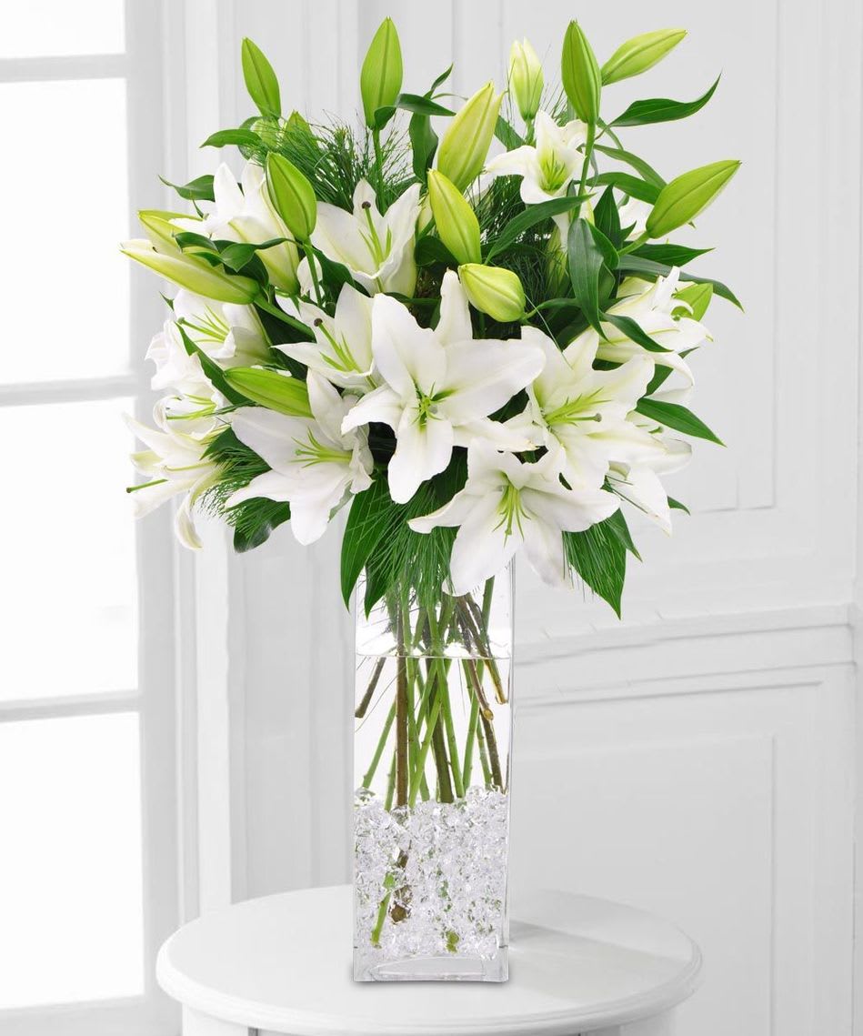White lilies arranged in a tall clear vase with green buds