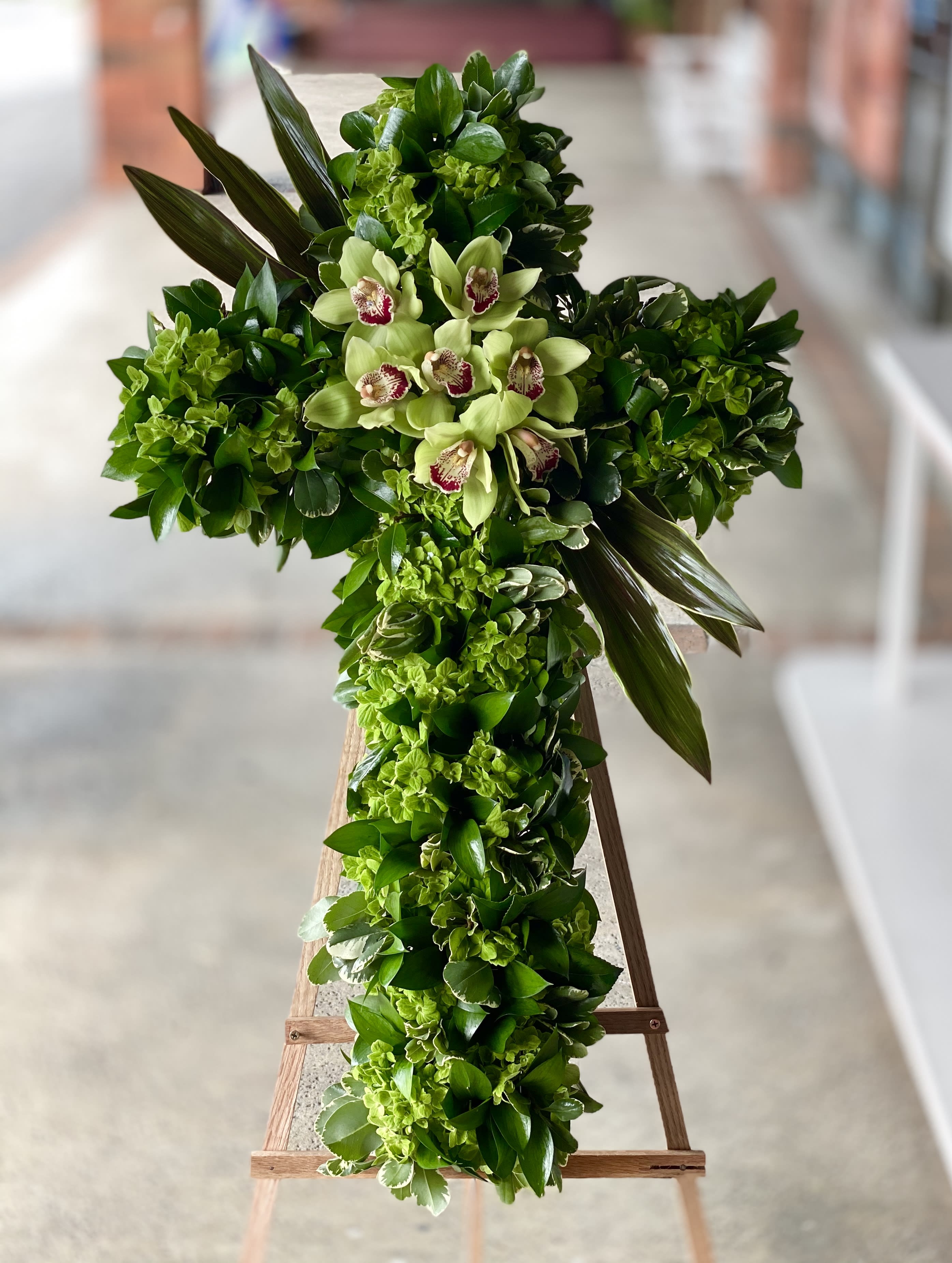 Green floral cross with pale orchids on a stand