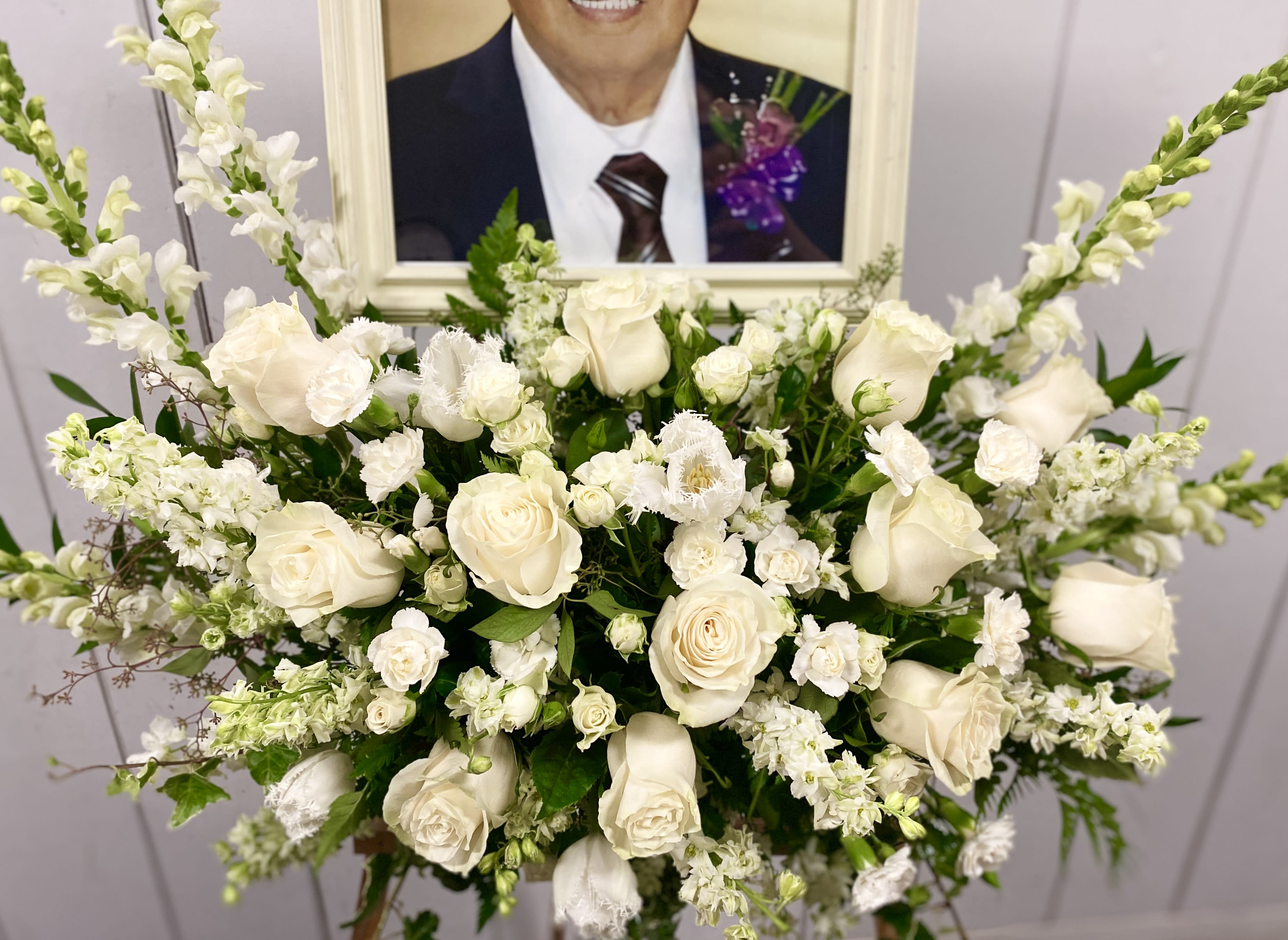White rose and snapdragon arrangement in front of a framed portrait