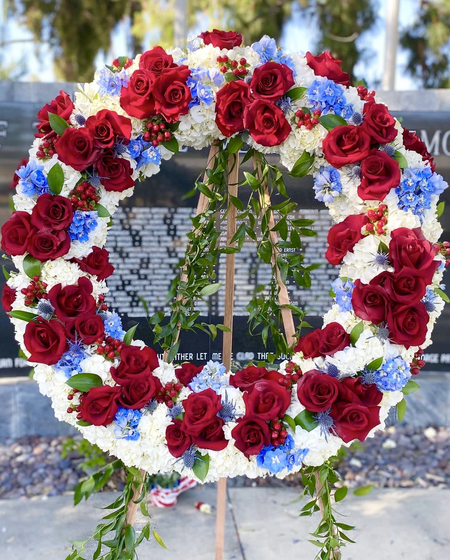 Large floral wreath of red roses, white blooms, and blue flowers on an easel
