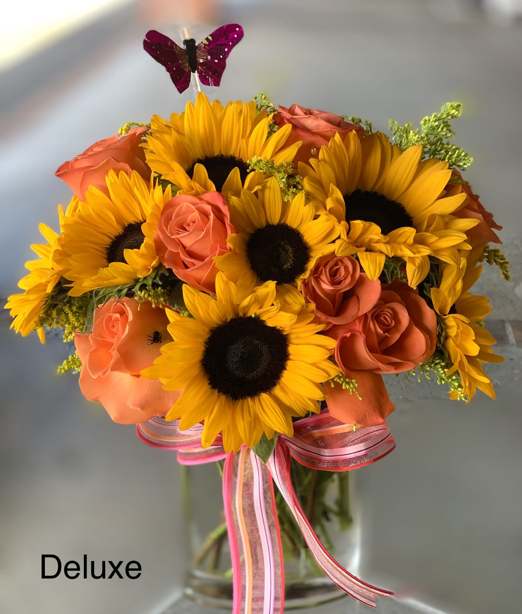 Sunflower and orange rose bouquet in a glass vase with pink ribbon
