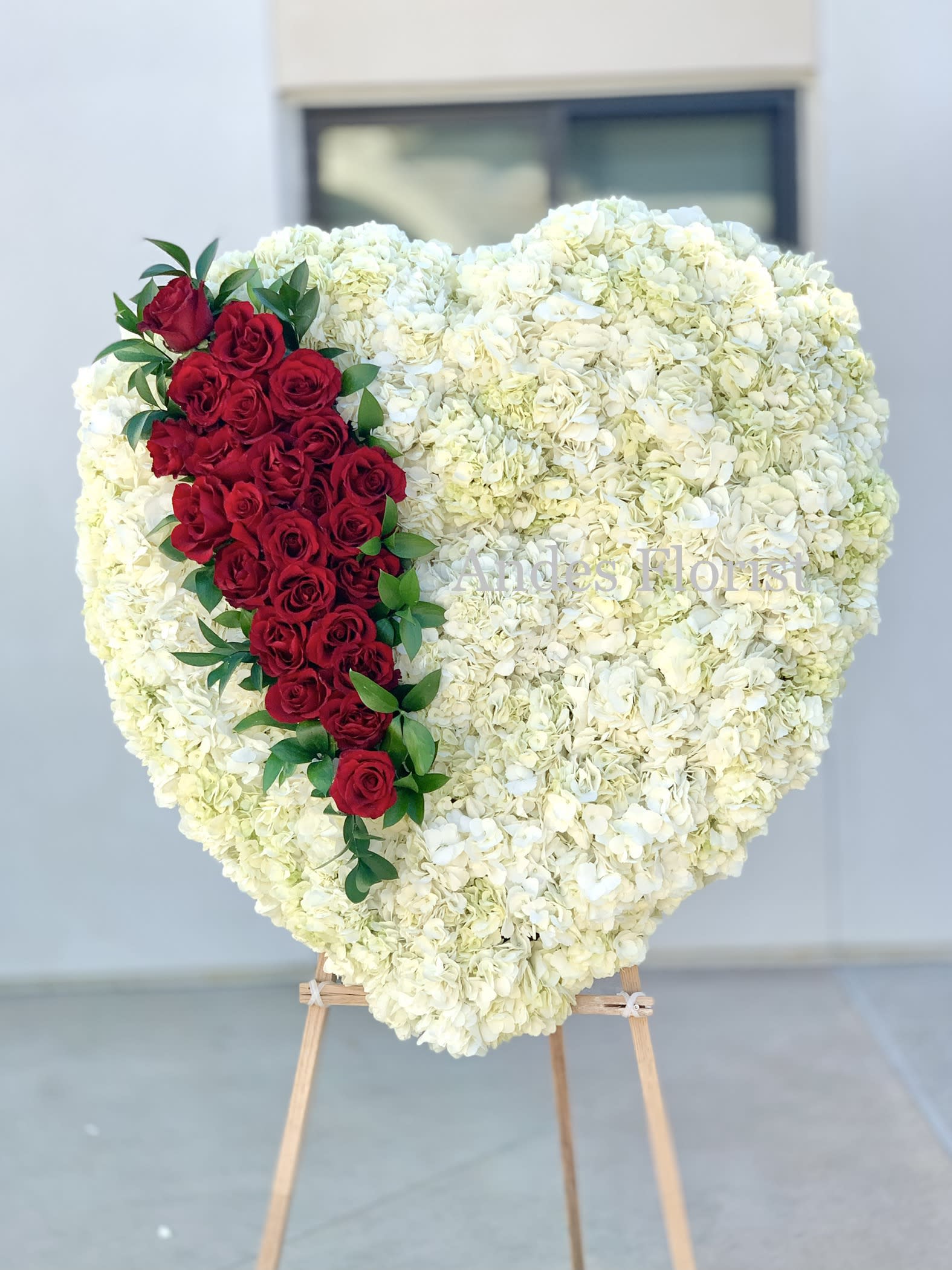 Heart-shaped white floral arrangement with a red rose cascade