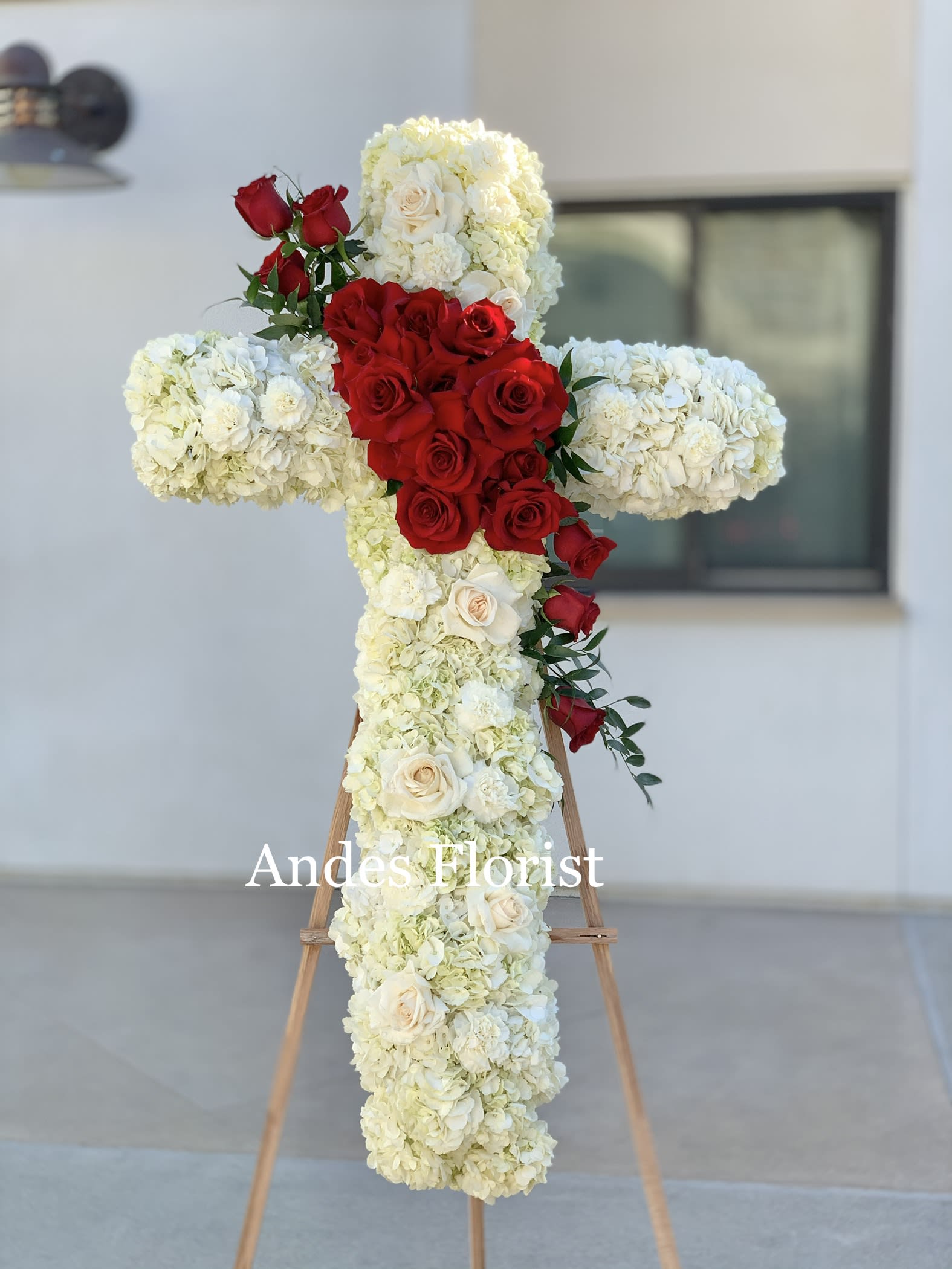 Cross-shaped floral tribute with red and white roses on an easel