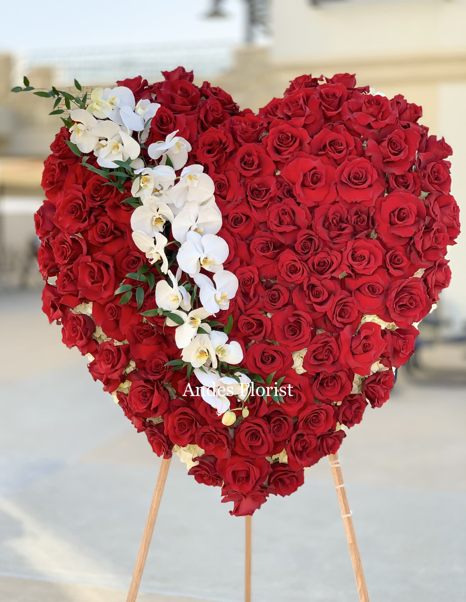 Heart-shaped red rose arrangement with white orchids on an easel