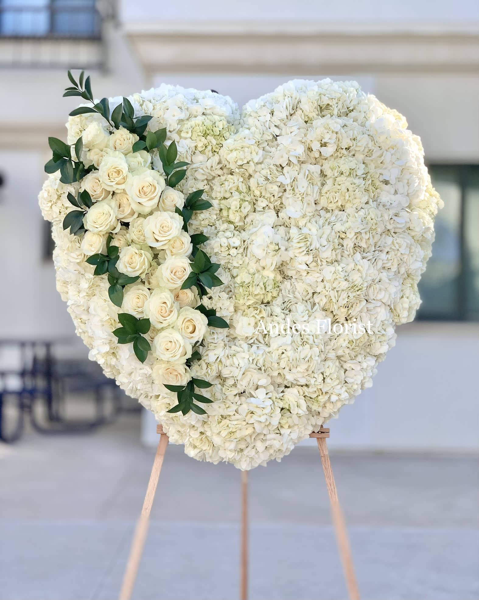 Heart-shaped white floral arrangement with cream roses and greenery