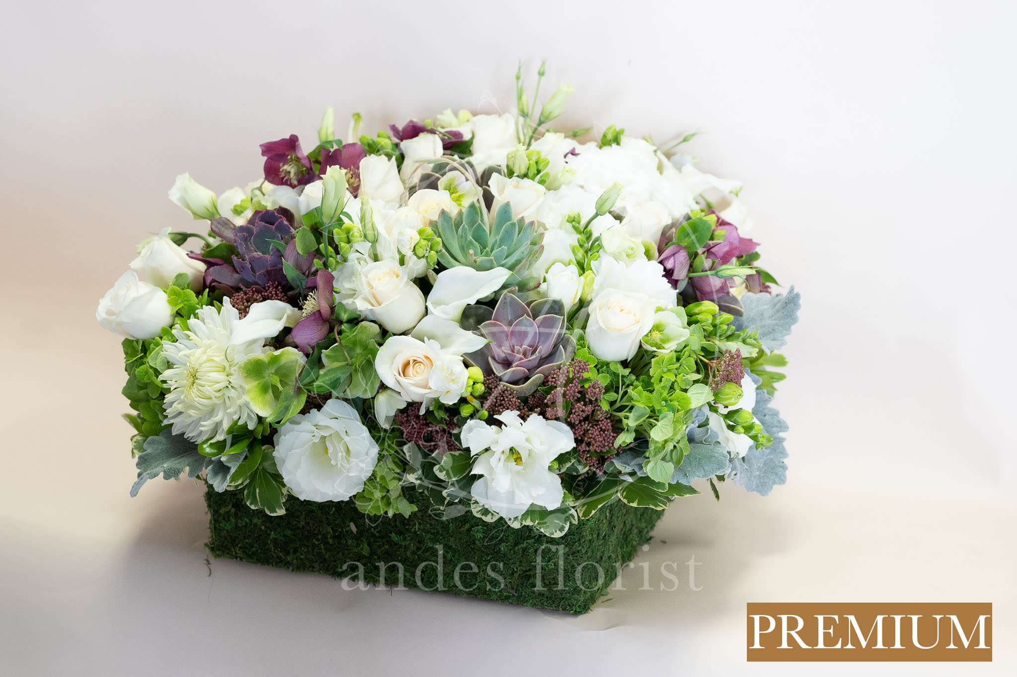 White and purple floral arrangement in a rectangular moss-covered container