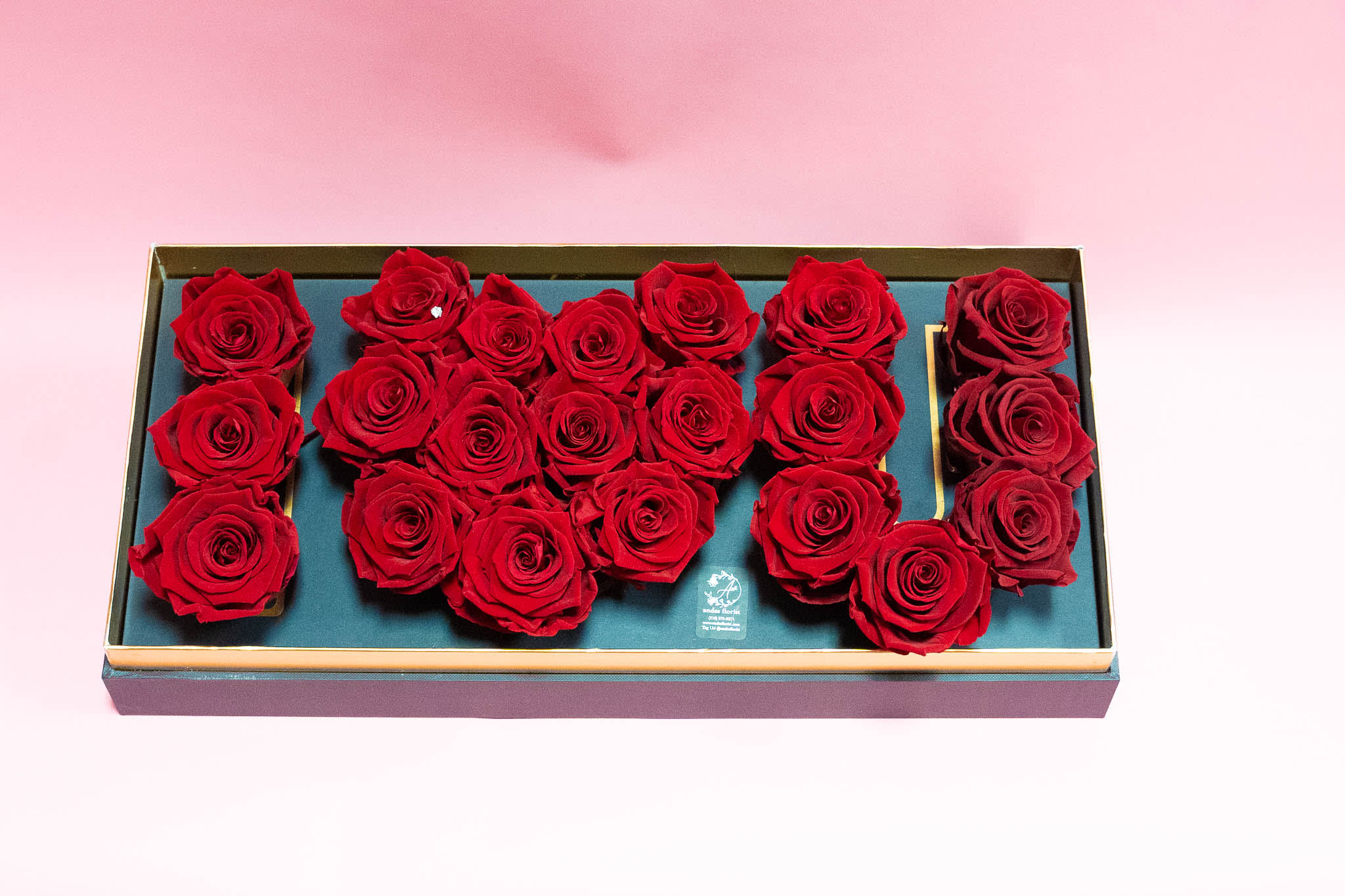 Red roses arranged in a rectangular gift box on a pink background