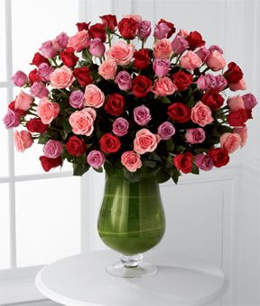 Bouquet of red, pink, and lavender roses in a green glass vase