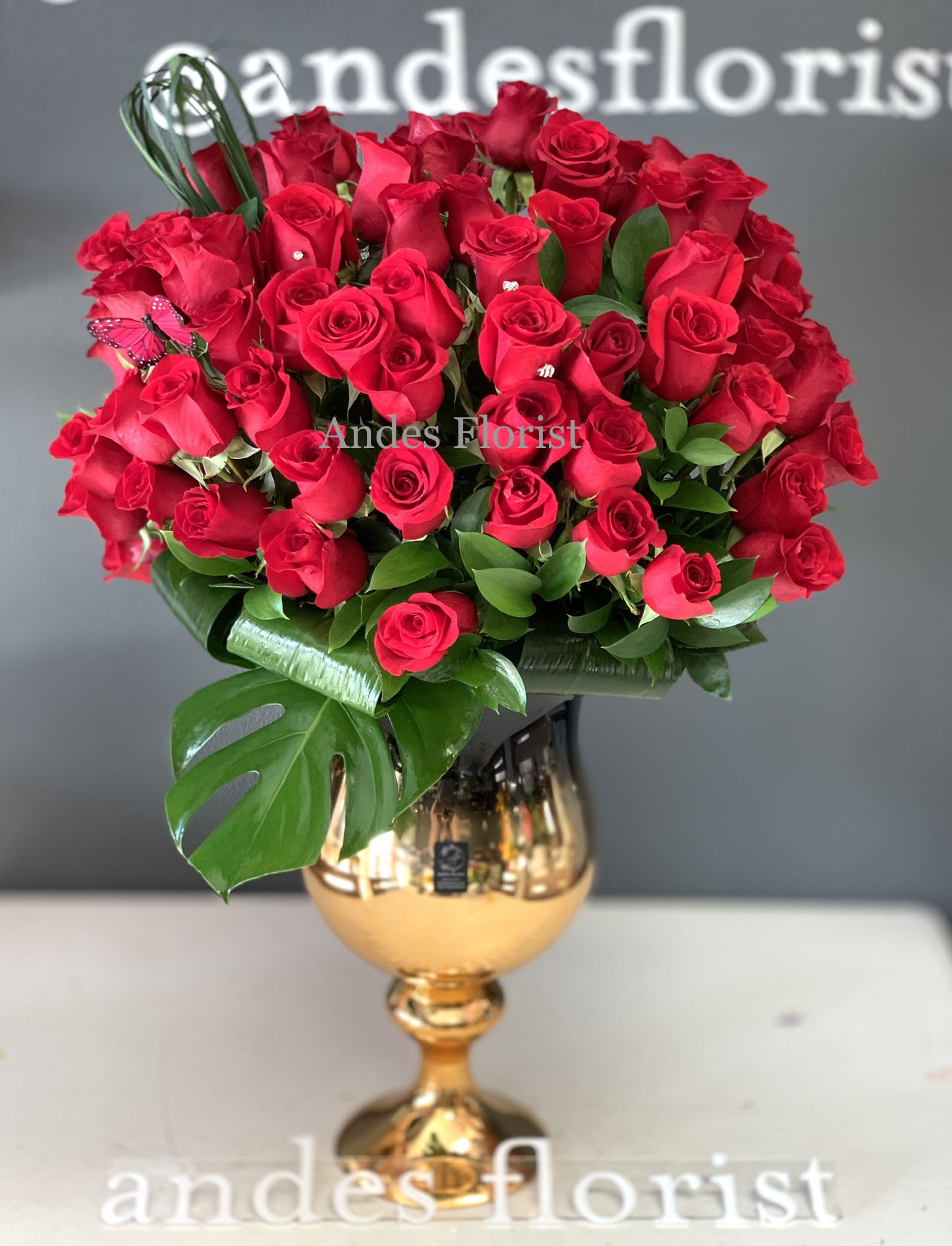 Red rose bouquet in a gold vase with large green leaves