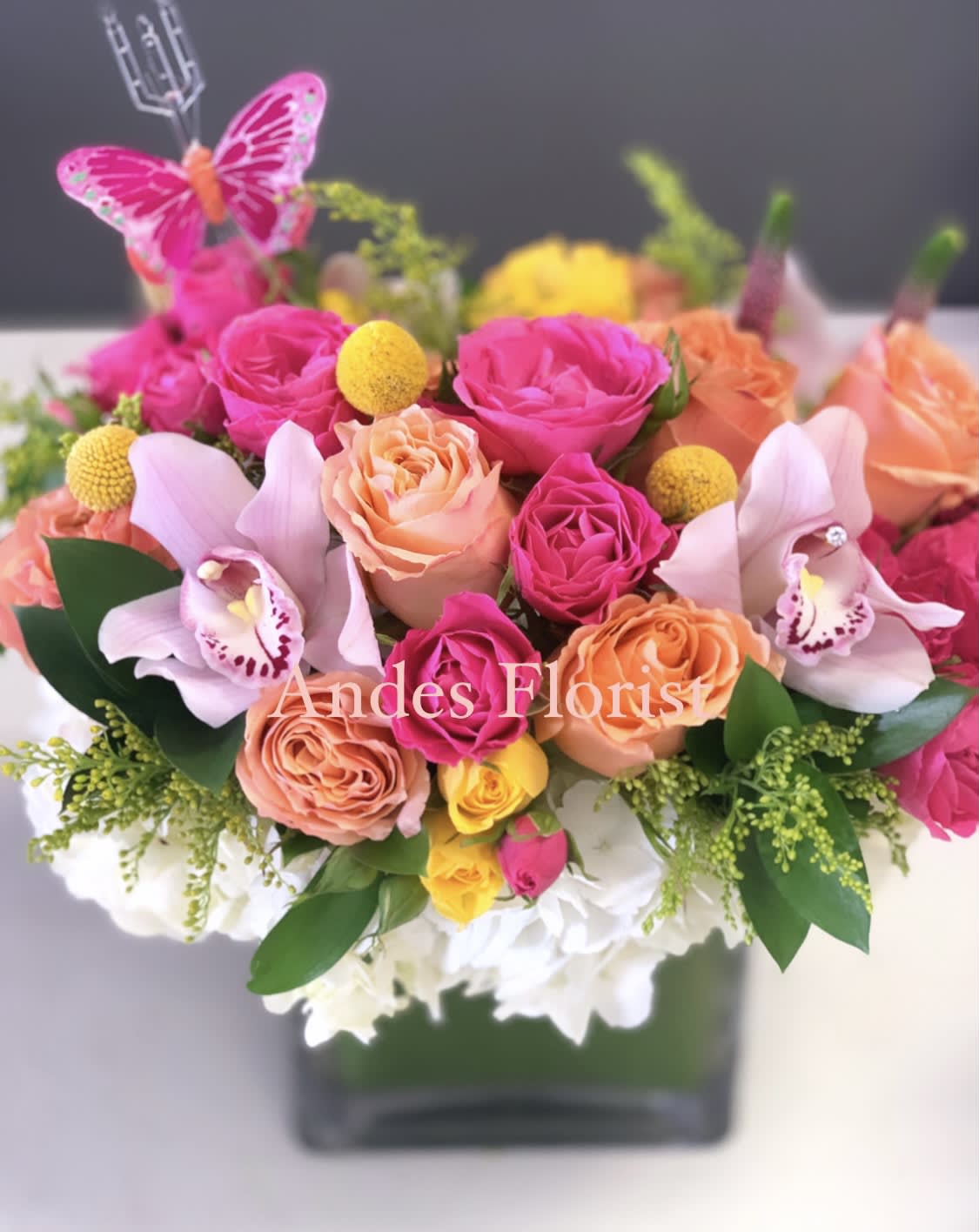 Bright pink and peach rose arrangement with orchids in a square vase