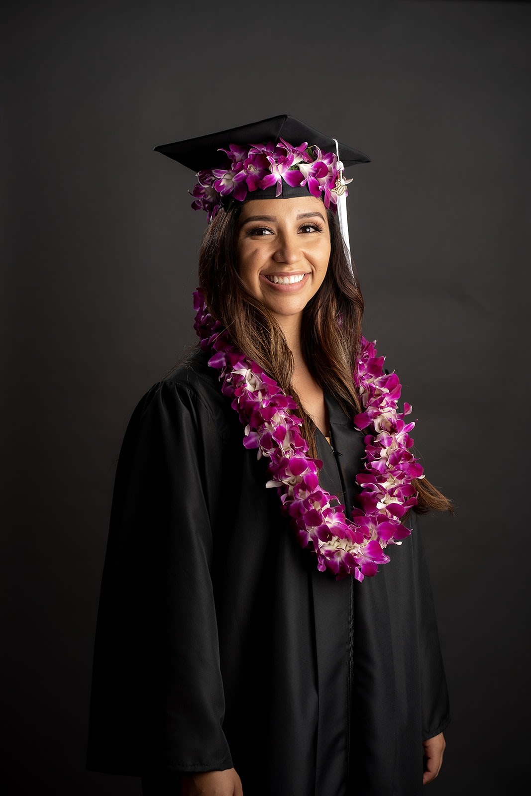 Graduate in a cap and gown wearing a purple orchid lei and matching cap flowers
