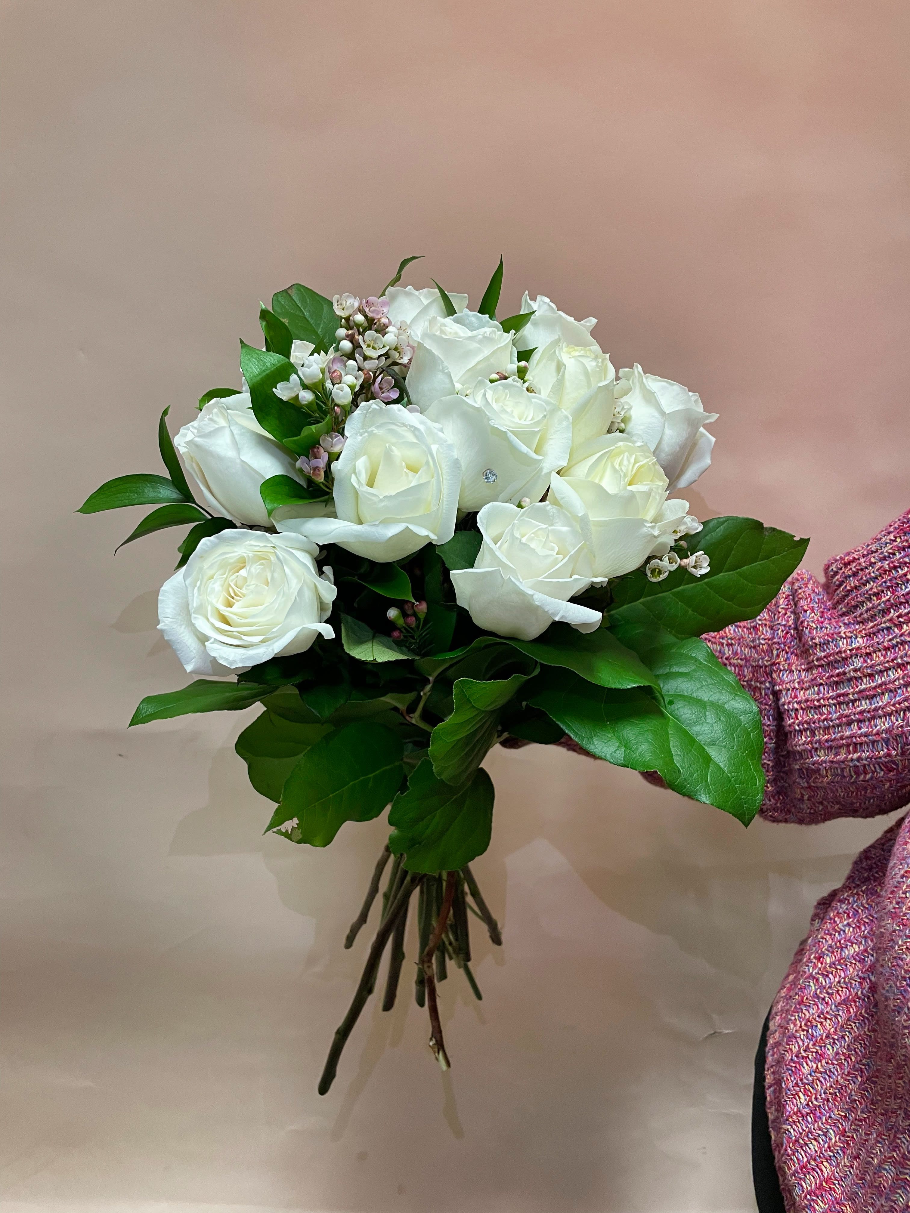 Bouquet of white roses with green foliage and small pink filler flowers