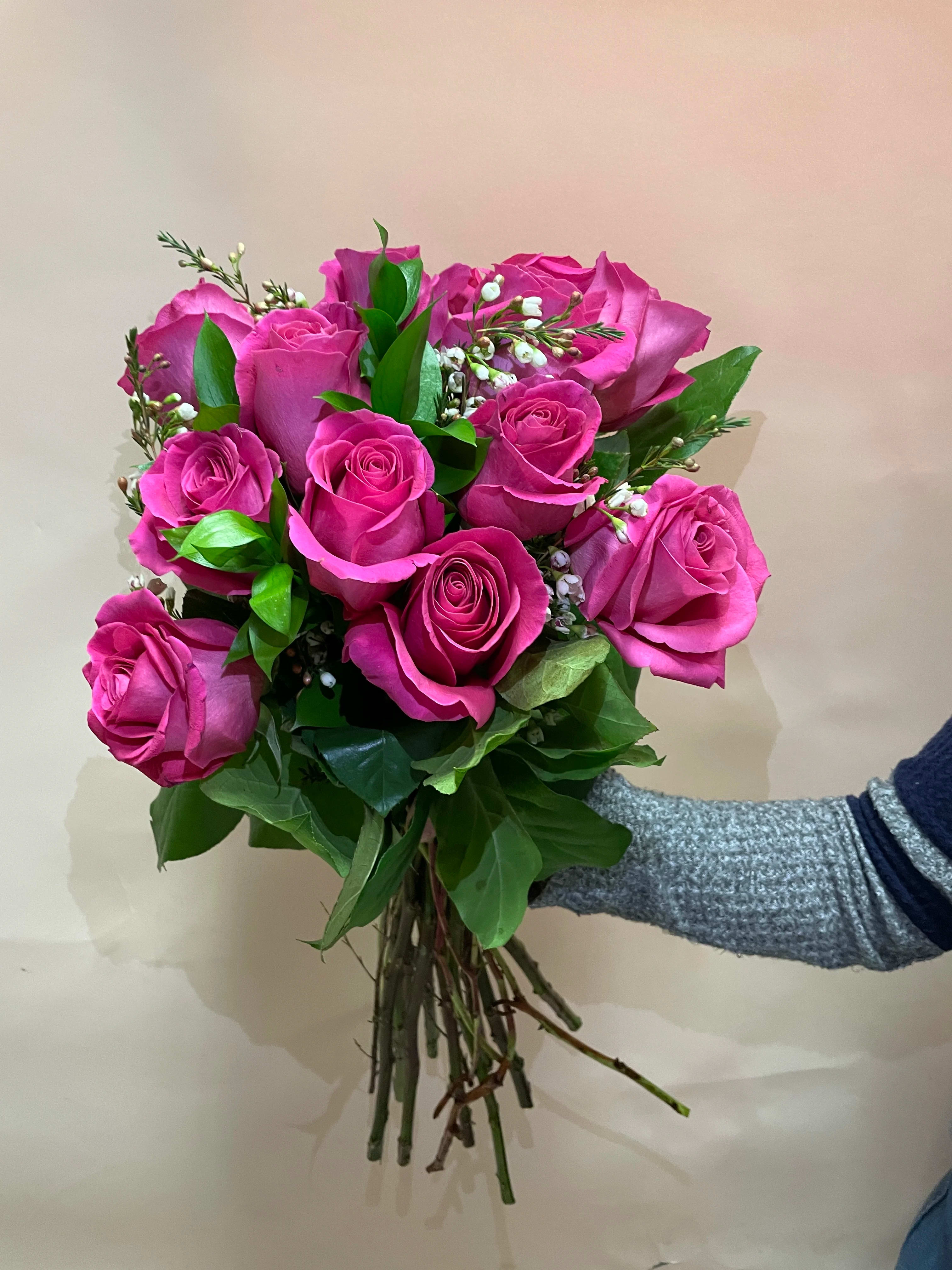 Handheld bouquet of bright pink roses with small white filler flowers