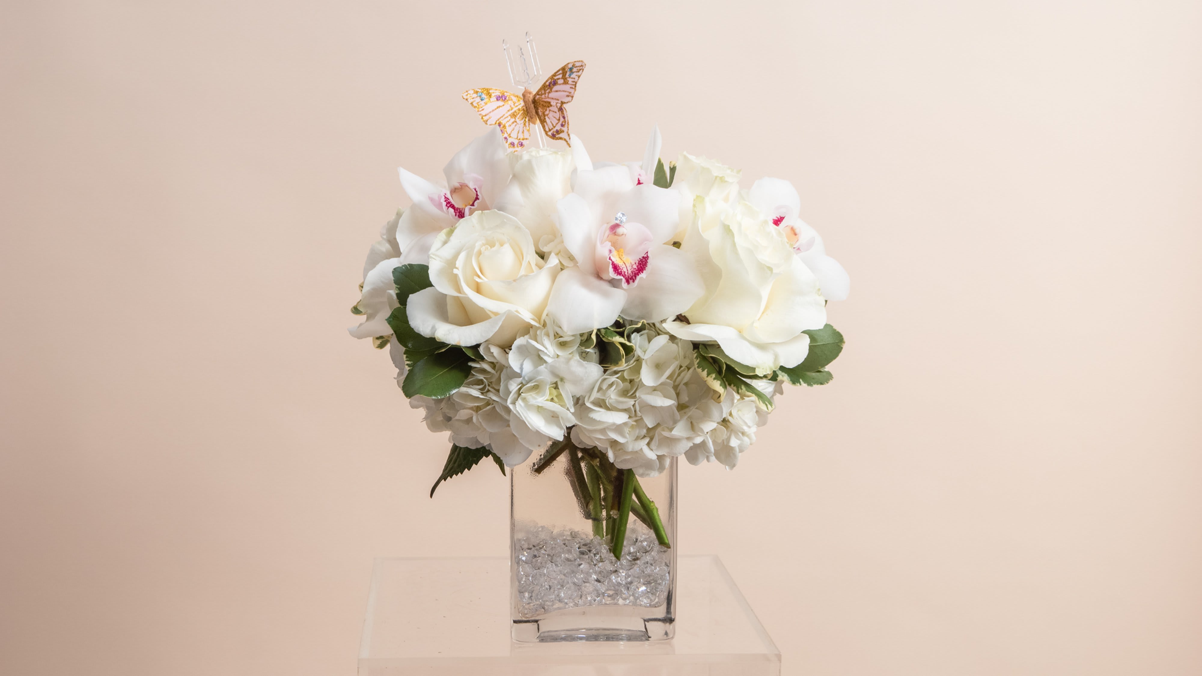 White floral arrangement in a clear square vase with a butterfly topper