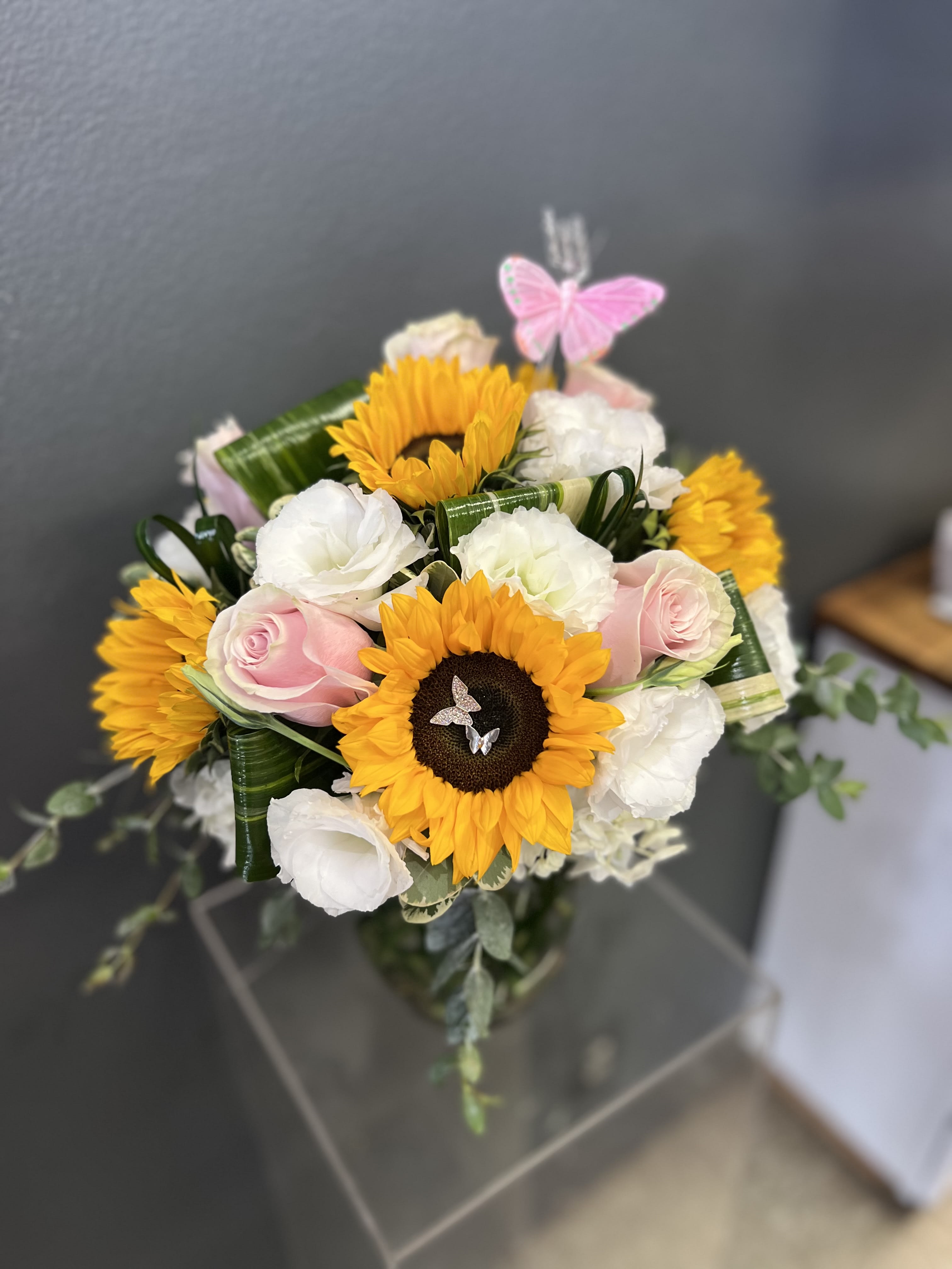 Bouquet of sunflowers, pink roses, and white blooms with a butterfly pick