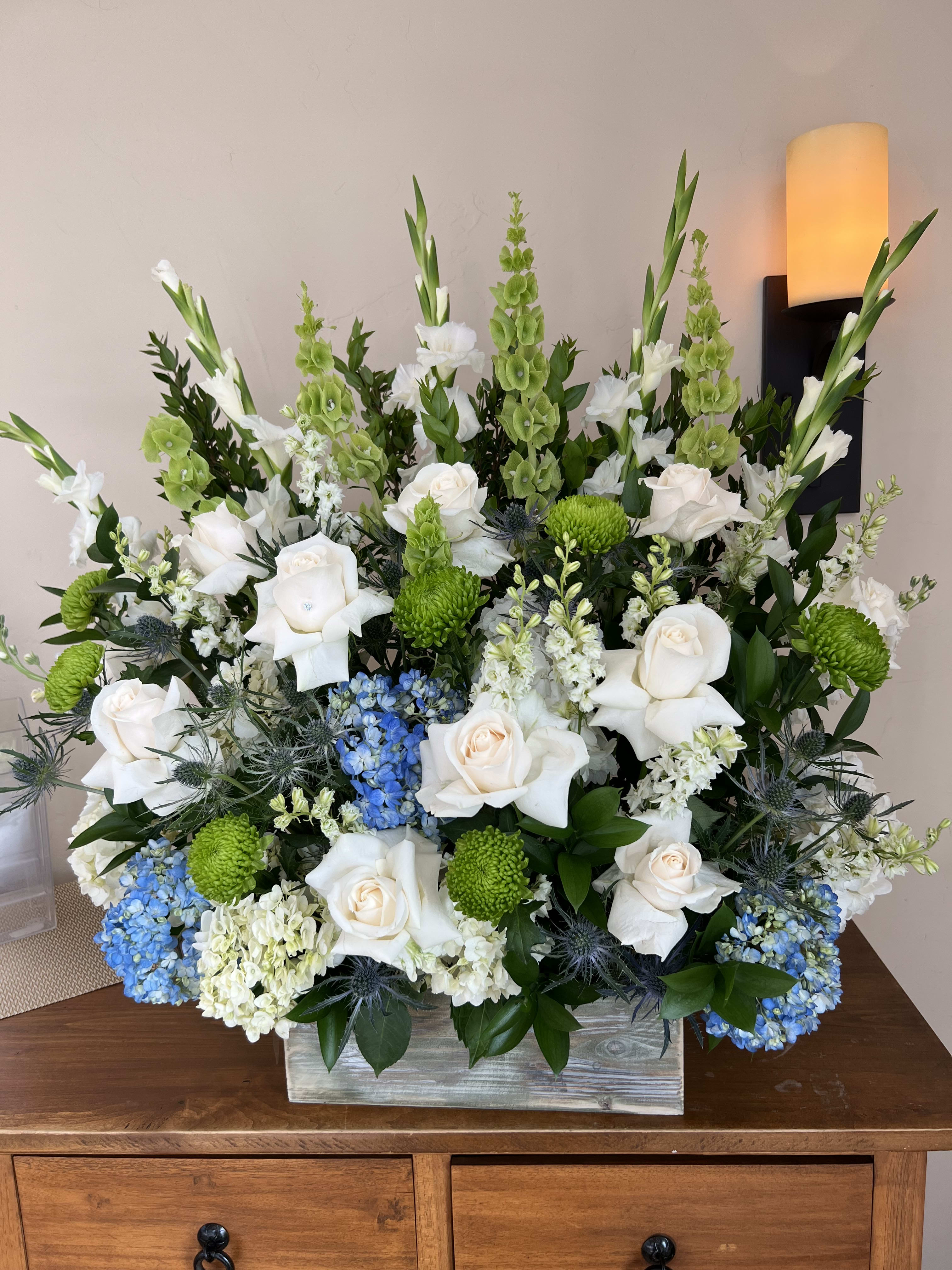 Large floral arrangement with white roses, green blooms, and blue hydrangeas in a wooden box