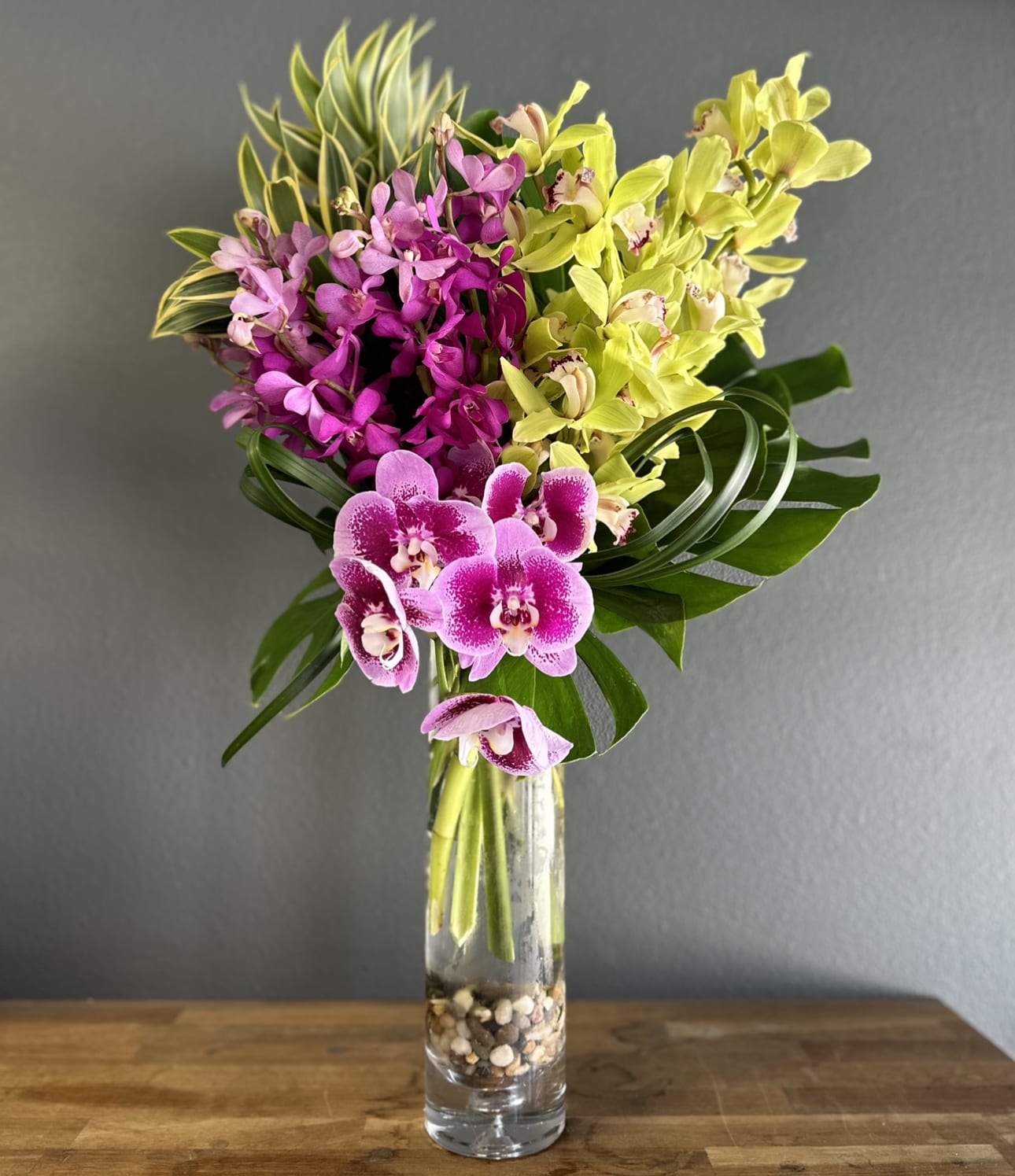 Pink and yellow orchids arranged in a tall glass vase.