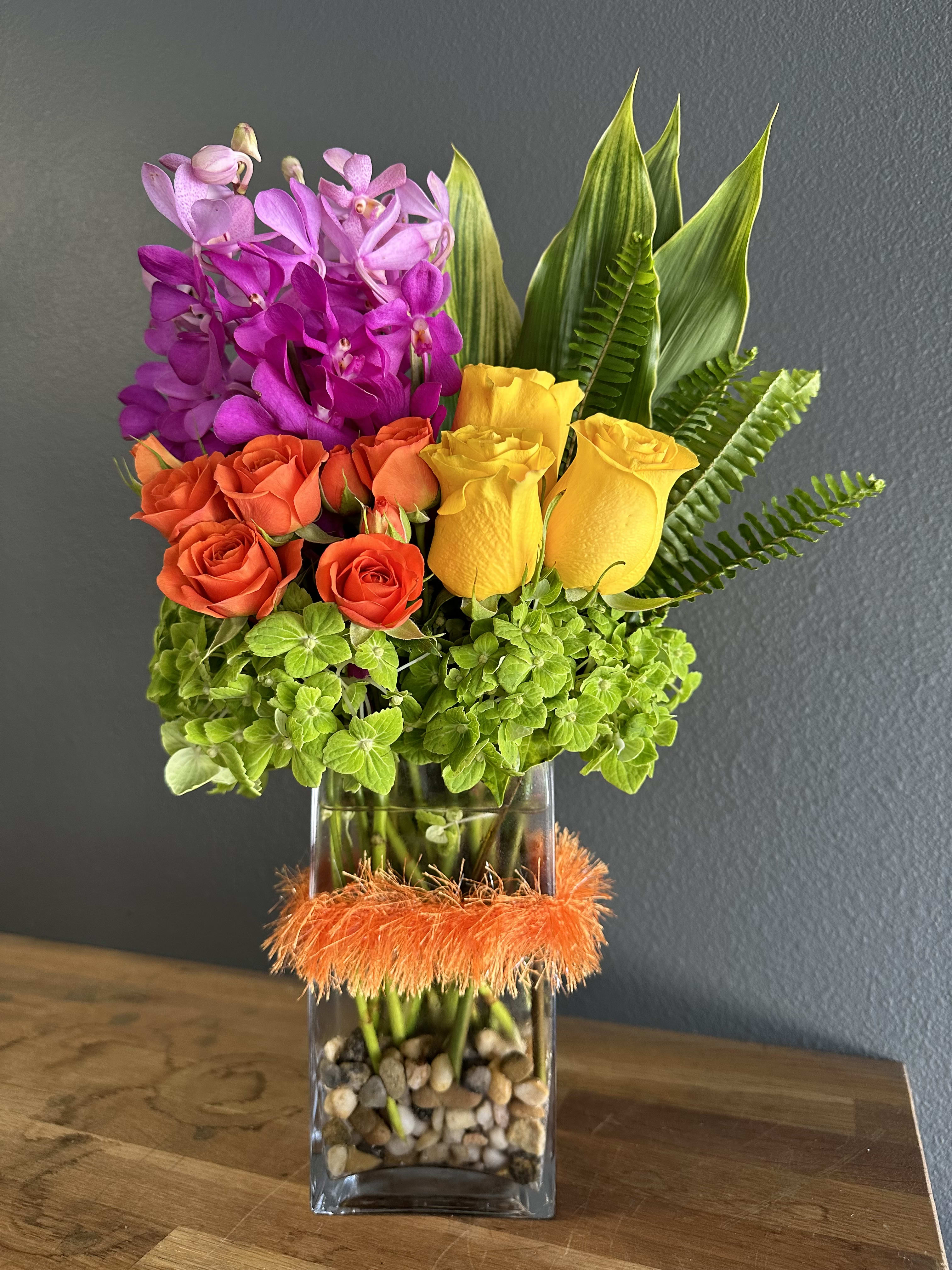 Colorful bouquet of orchids and roses in a glass vase with orange trim
