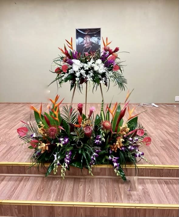 Large tropical floral tribute with white and purple flowers on a stand