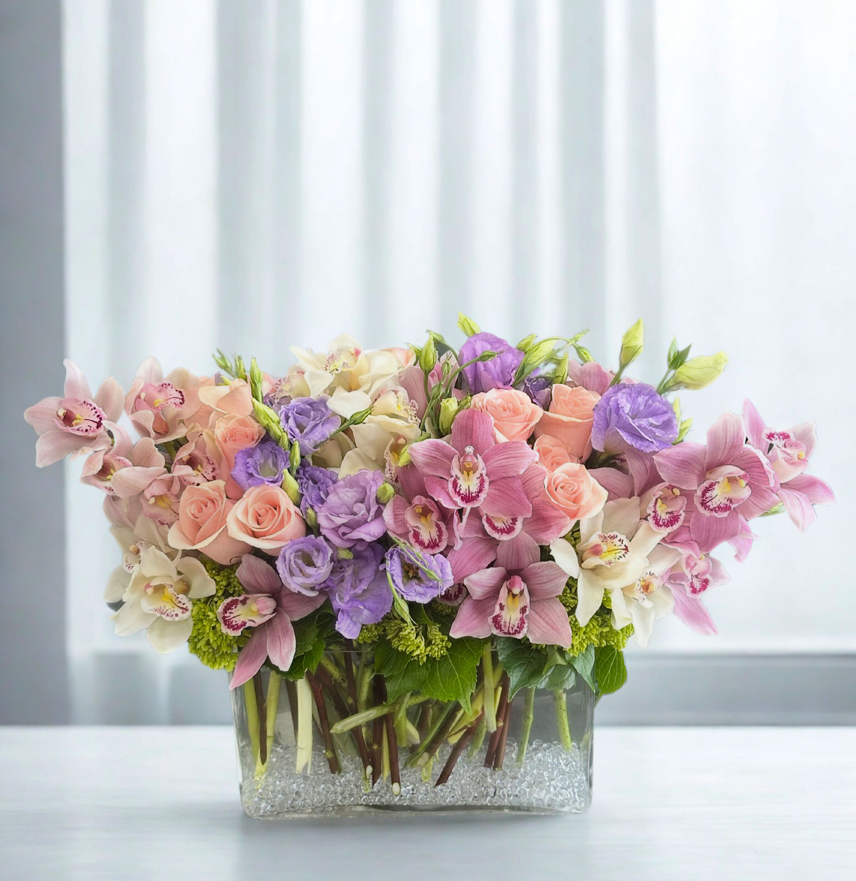 Arrangement of pink, purple, and white flowers in a clear rectangular vase