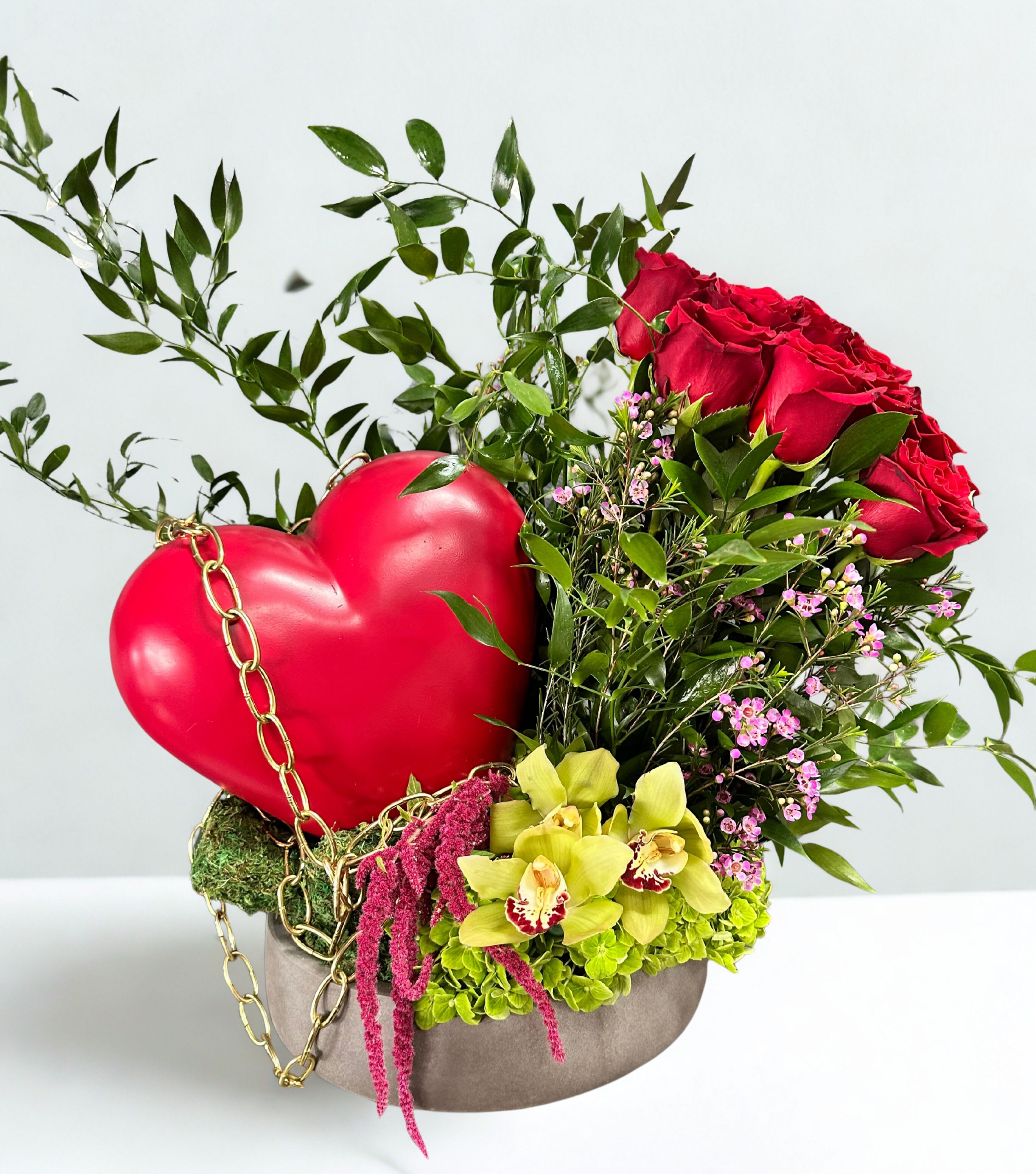 Red roses and orchids arranged with a heart decoration in a round box