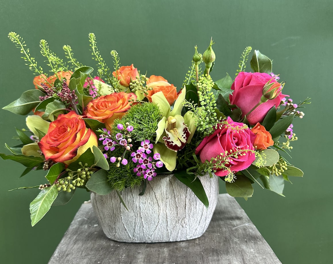 Mixed roses and orchids arranged in a white textured vase