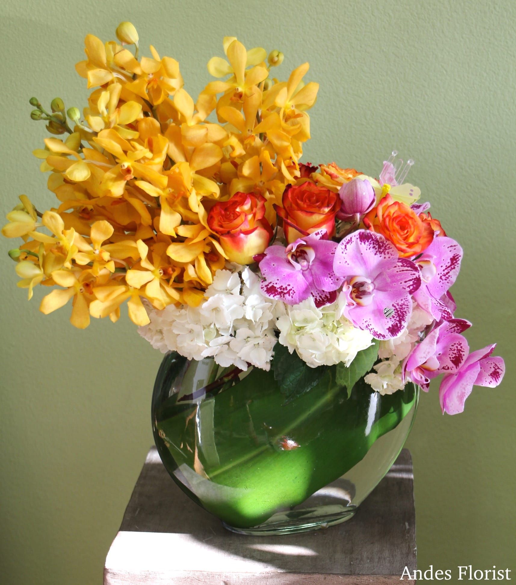 Yellow orchids, pink orchids, roses, and white hydrangeas in a glass vase