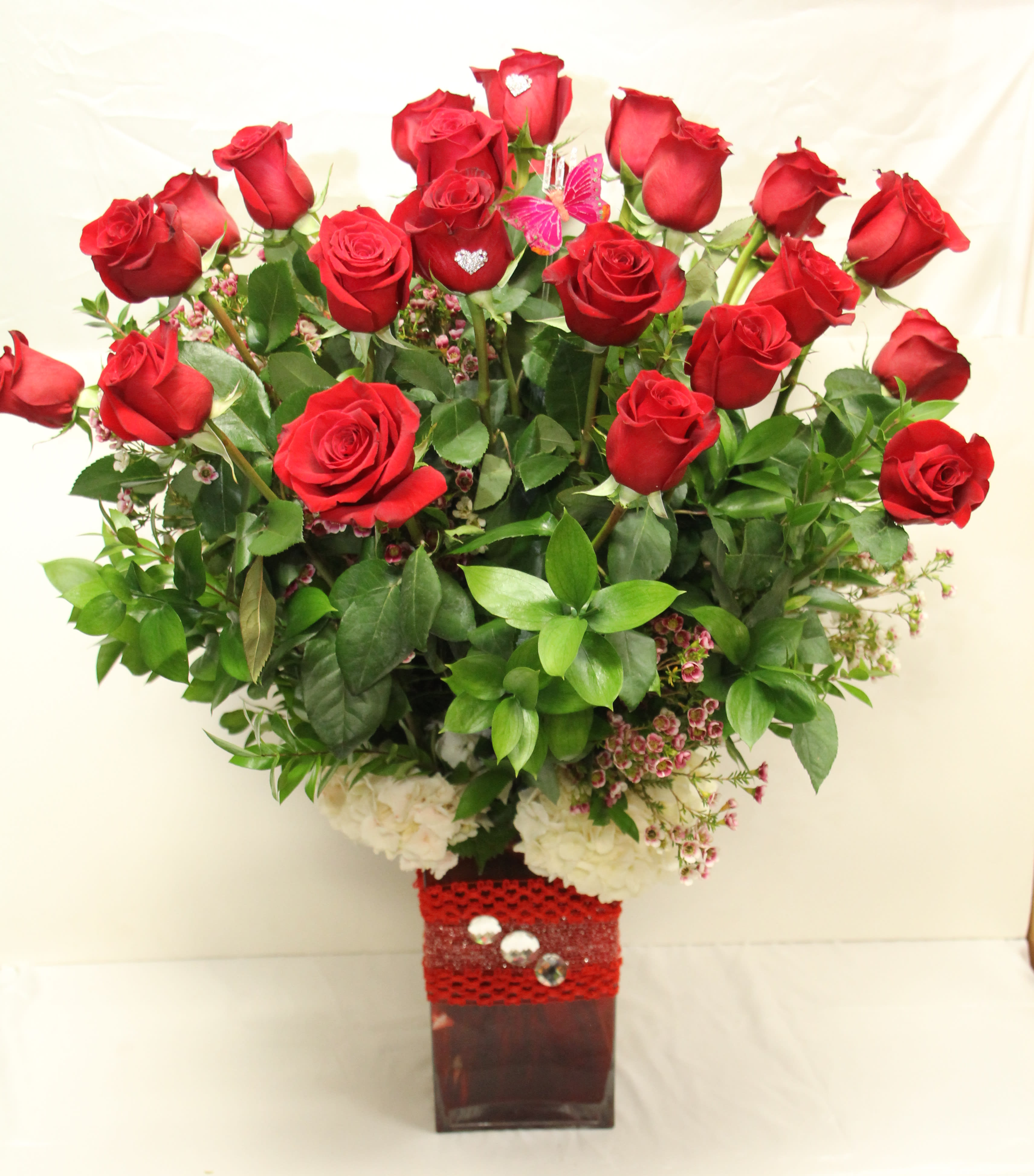 Red roses arranged in a square vase with greenery and white flowers