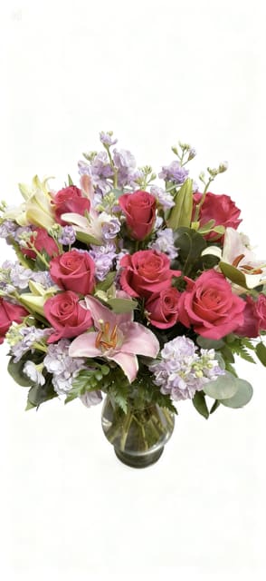 Pink roses and lilies arranged in a glass vase with lavender flowers