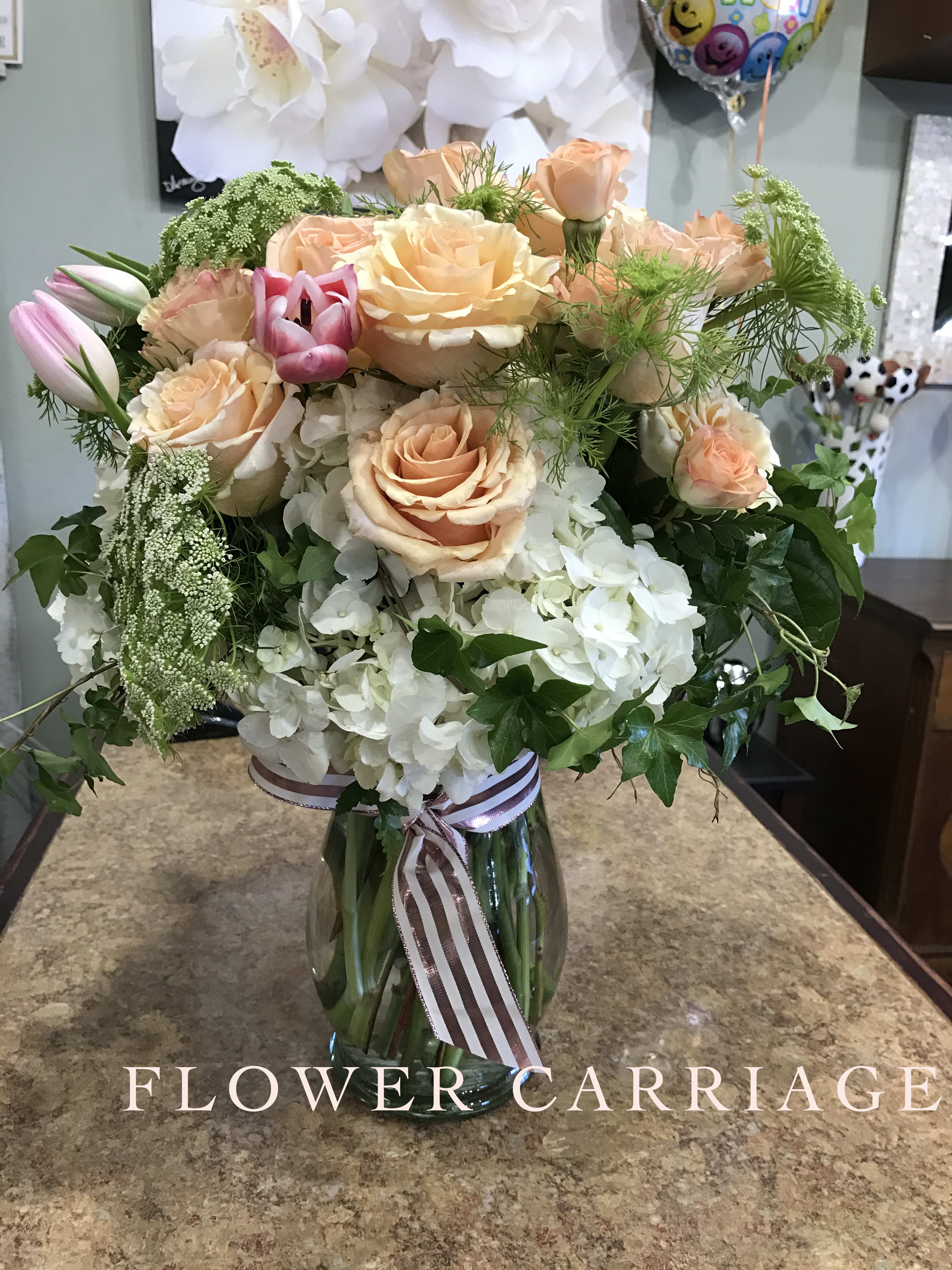 Peach roses and white hydrangeas in a glass vase with ribbon