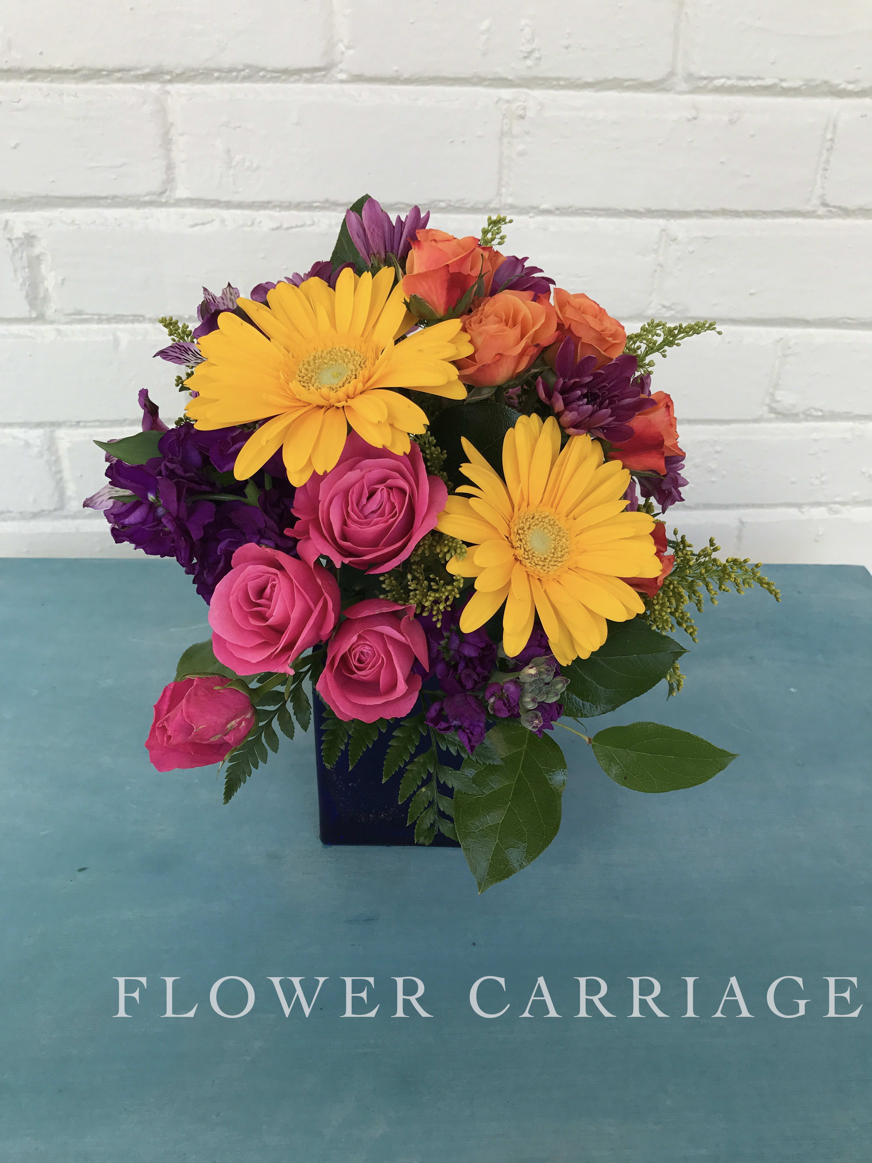 Bright mixed bouquet with yellow daisies, pink roses, and purple flowers in a dark vase