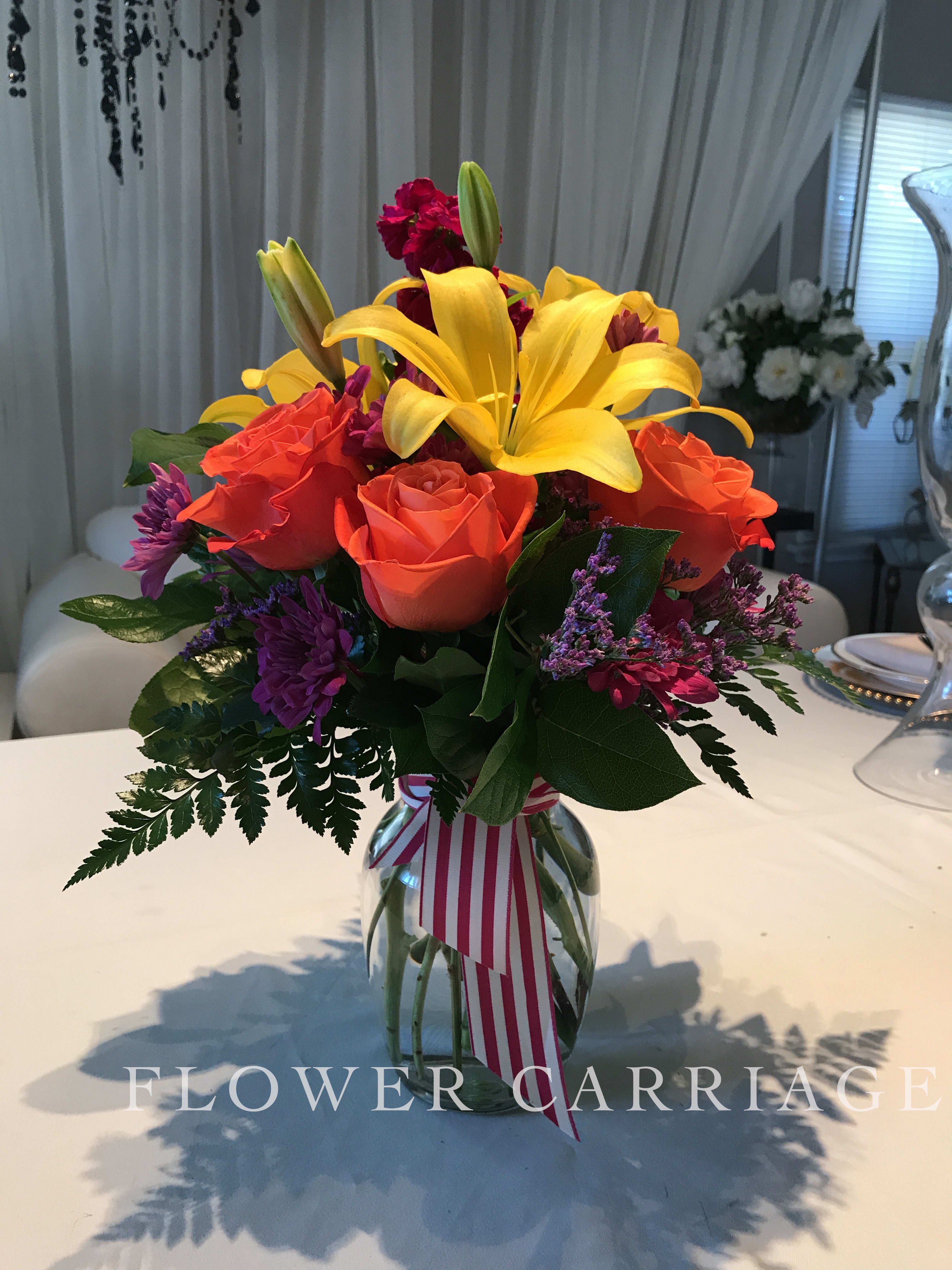 Bouquet of yellow lilies, orange roses, and purple flowers in a glass vase