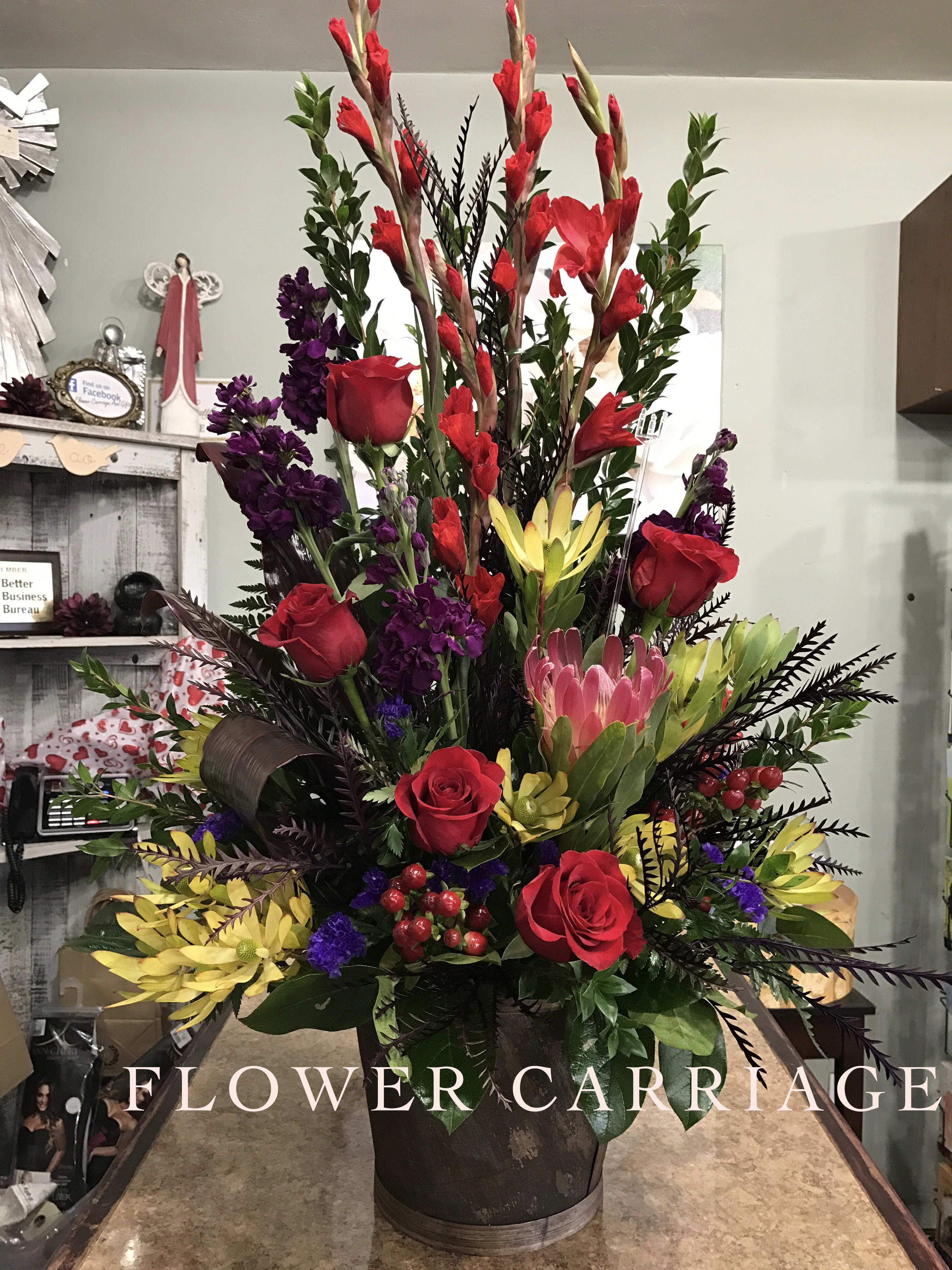 Tall mixed floral arrangement with red roses, purple blooms, and yellow flowers in a dark container