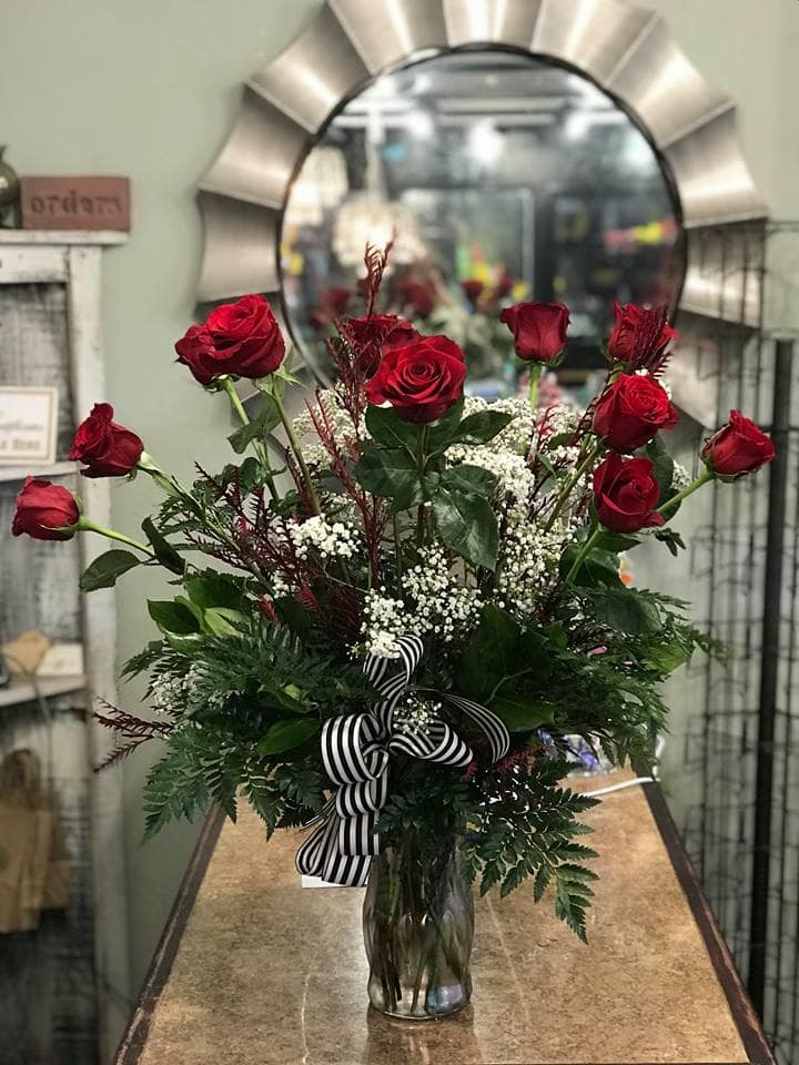 Red roses arranged in a clear glass vase with a striped ribbon