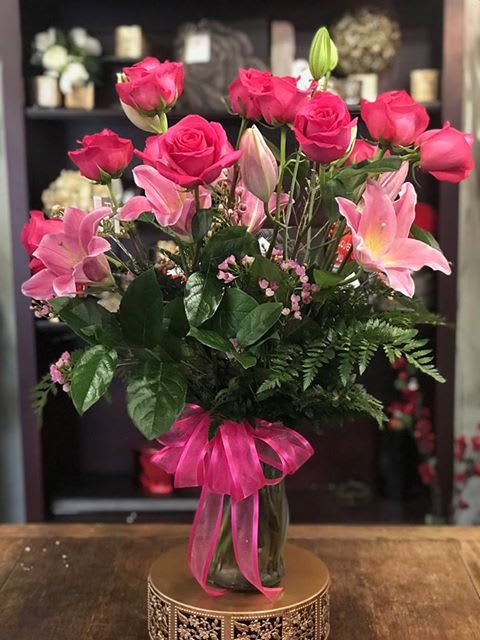 Pink roses and lilies arranged in a glass vase with a pink ribbon