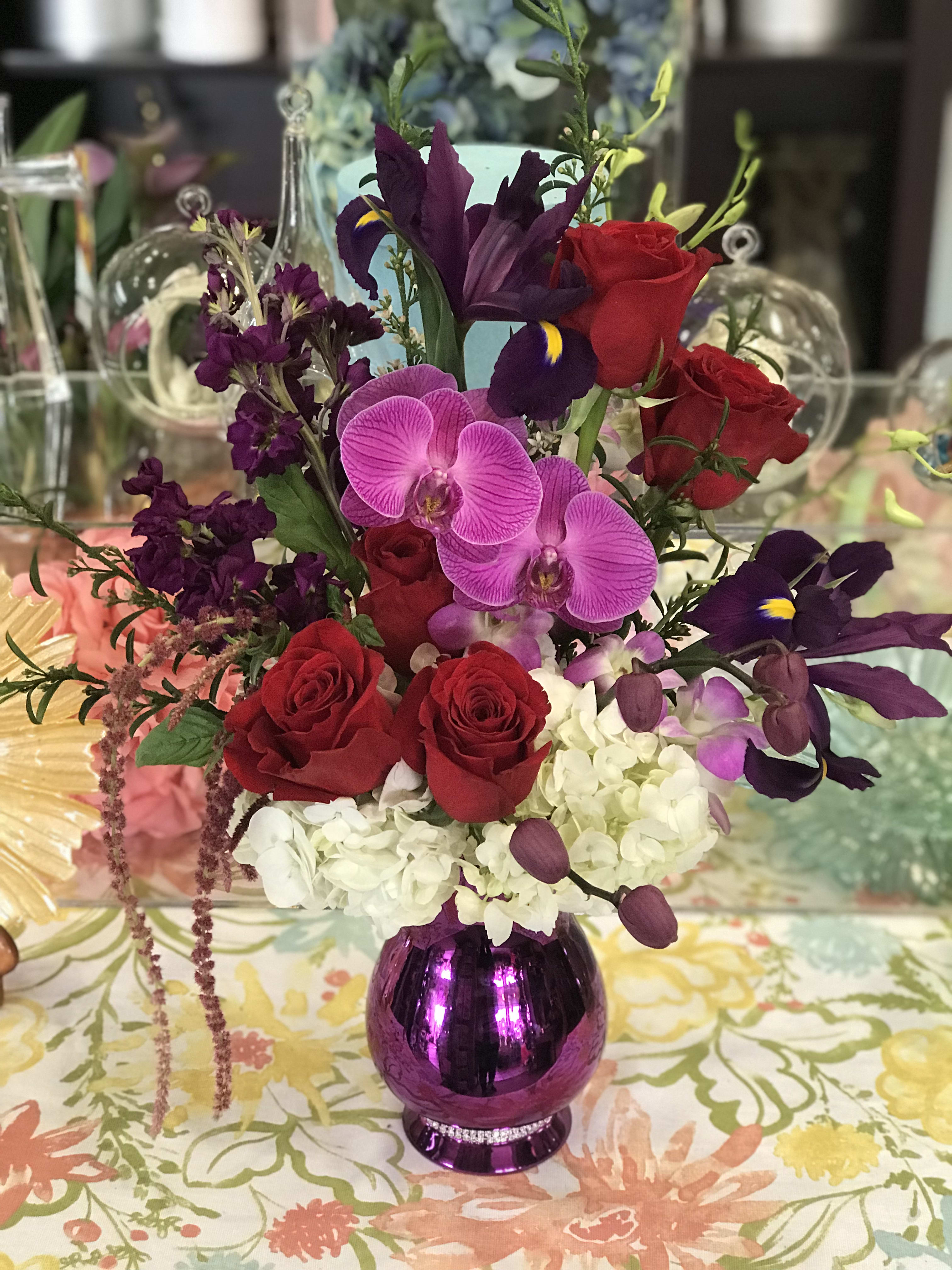 Mixed bouquet of red roses, purple orchids, and white hydrangea in a purple vase