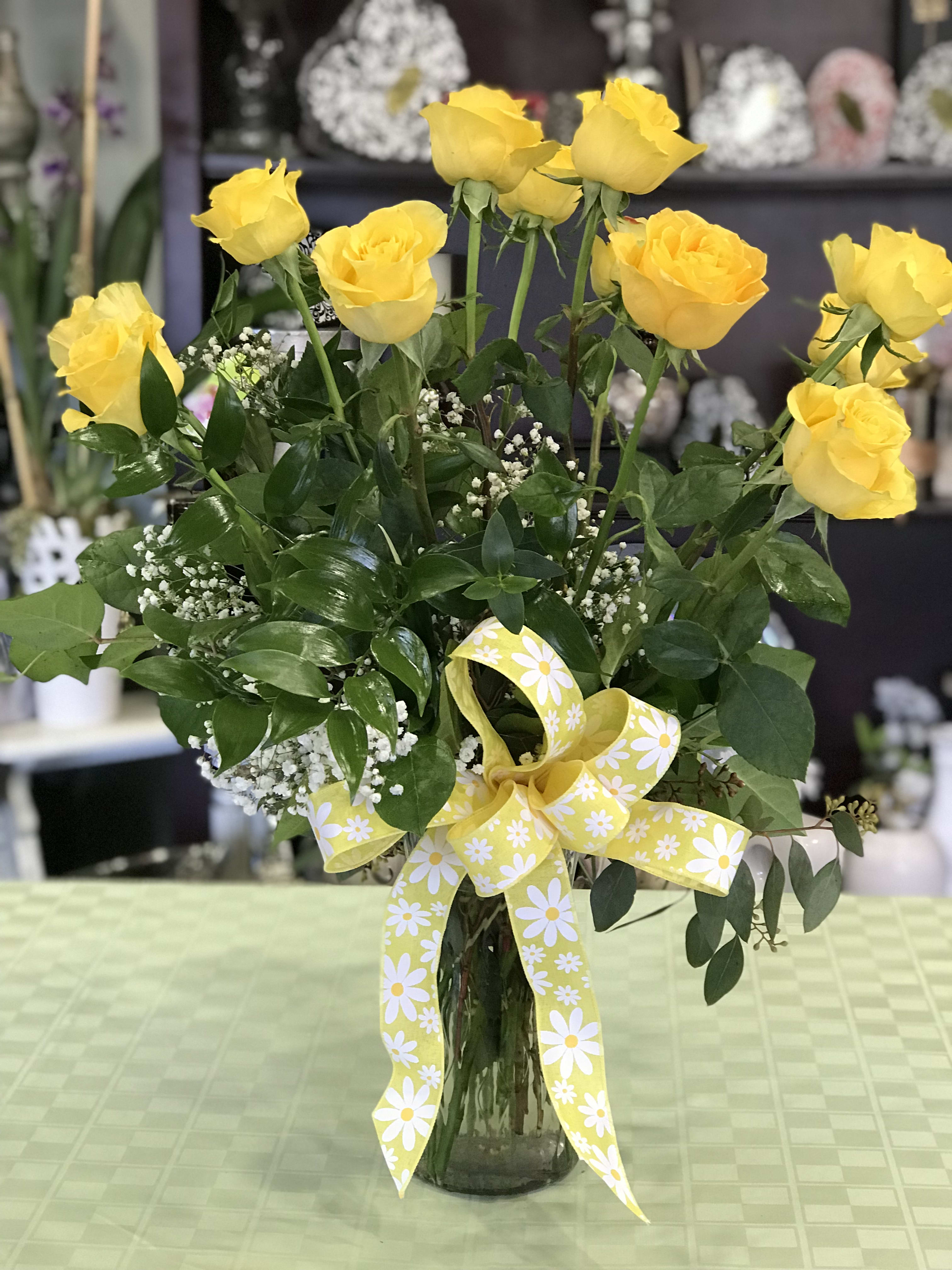 Yellow roses in a glass vase with a yellow daisy ribbon